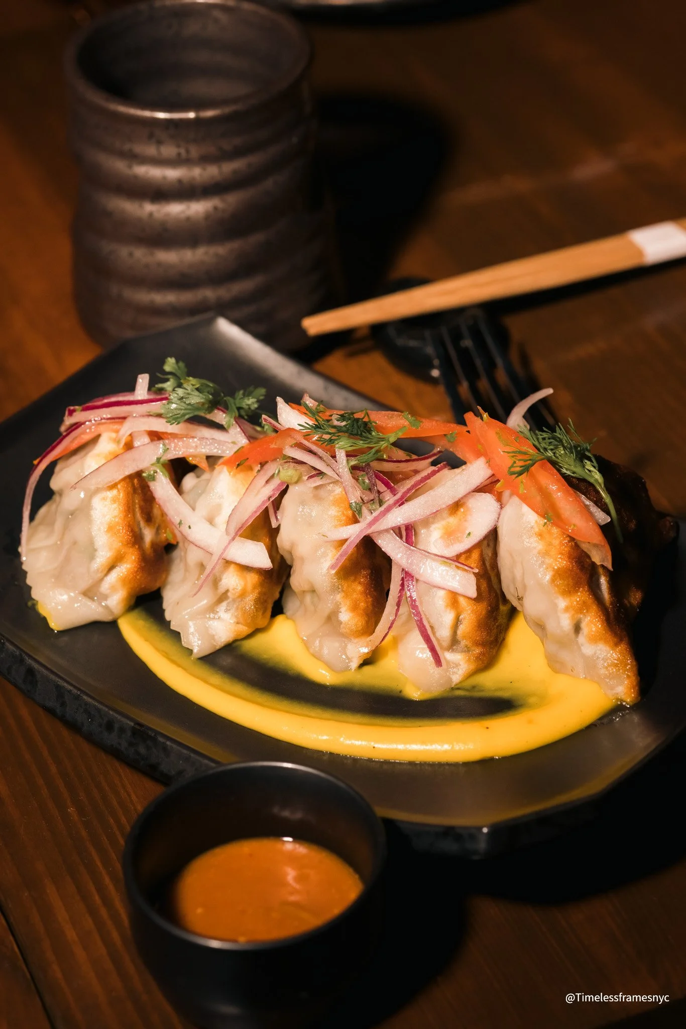 Plate of Japanese gyoza dumplings topped with sliced onions, herbs, and tomatoes, served with dipping sauce on the side.