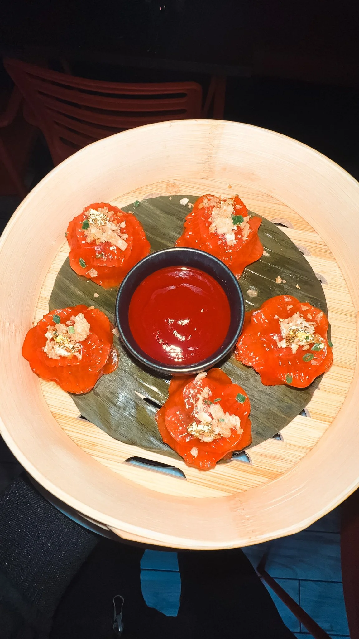 Bamboo steamer basket containing six pieces of salmon sashimi topped with green onions, garlic, and seasonings, served with soy sauce in a small black bowl.
