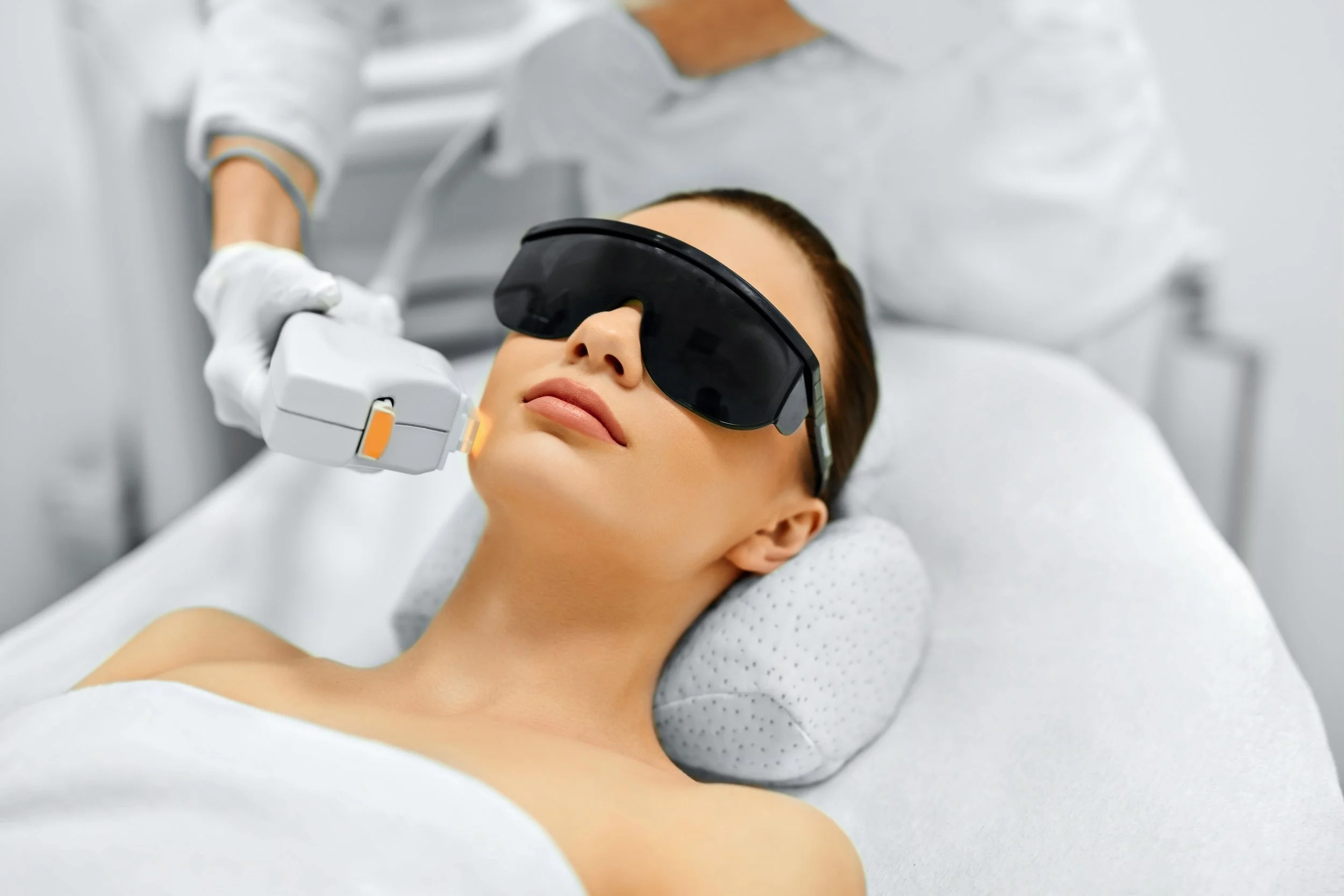A woman receiving a laser skin treatment while wearing protective goggles in a clinical setting.