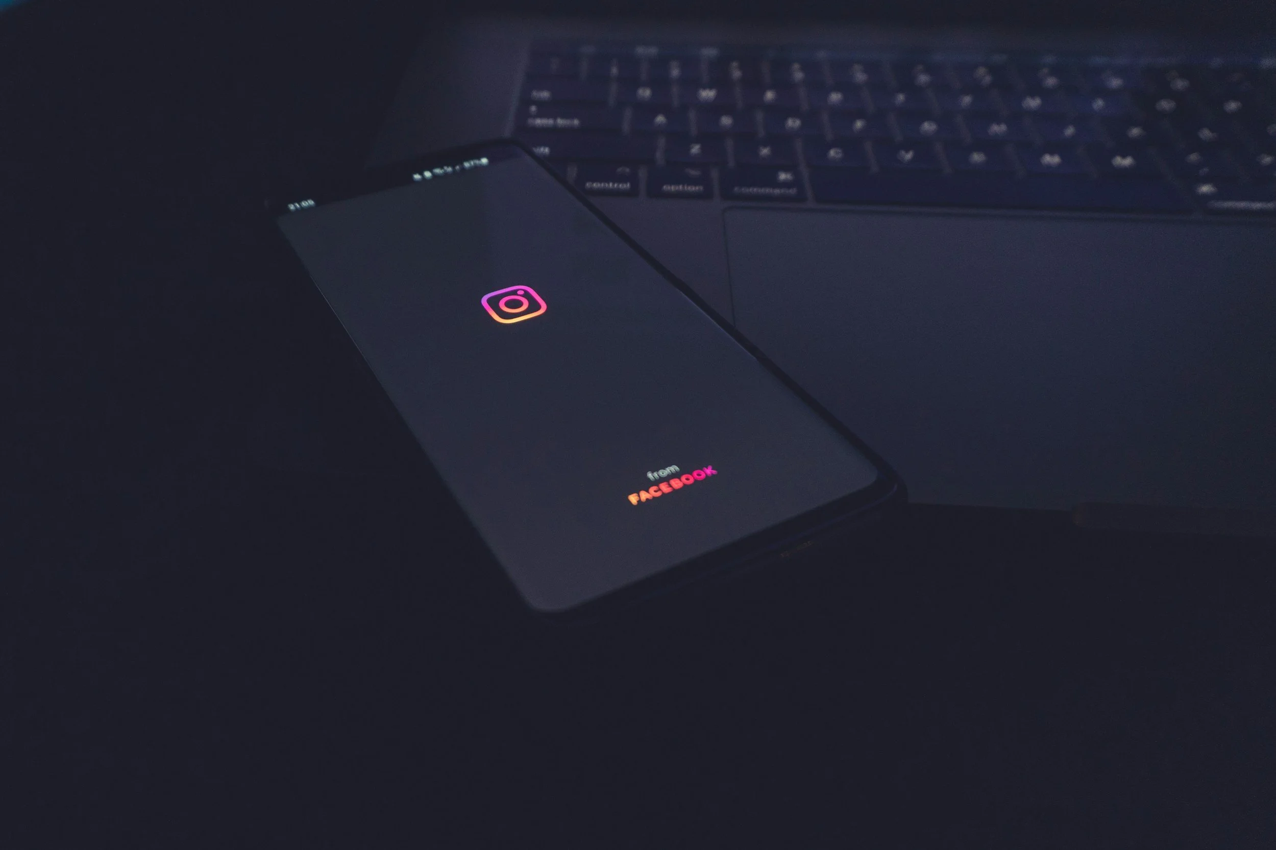 Smartphone displaying Instagram app logo on dark background, placed on a laptop keyboard in a low-light setting.