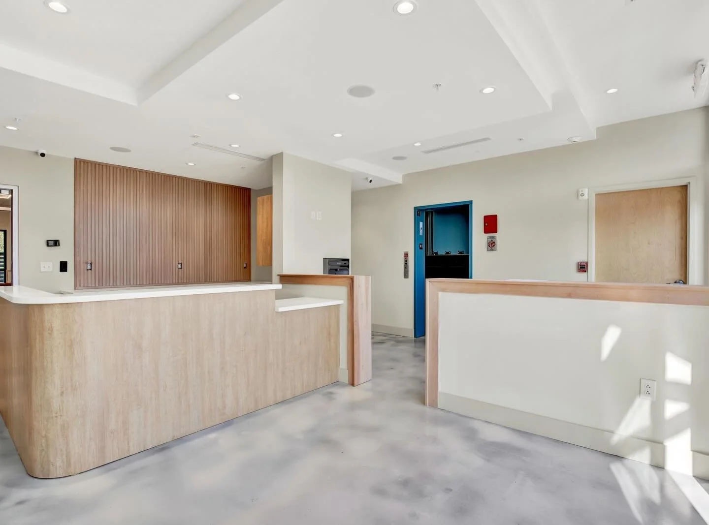 Interior view of a modern building lobby with a wooden reception desk for "A Place To Paws" Luxury Pet Boarding and Dog Daycare, a blue elevator door, and light-colored walls and flooring. in "PAWS Center"  facility in Bluffton, SC in the Lowcountry.