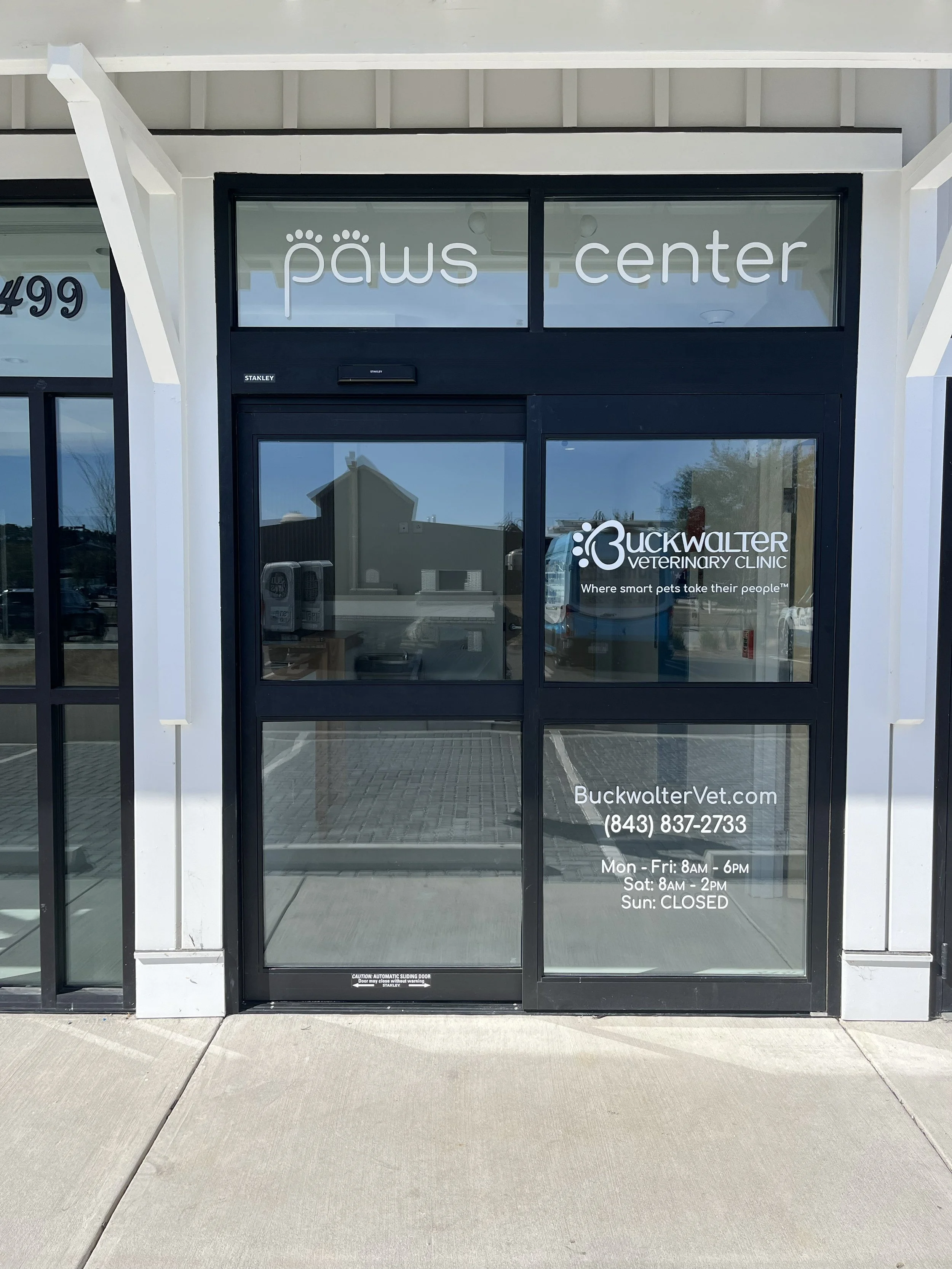 Glass door of Buckwalter Veterinary Clinic with business hours, phone number, website, and logo visible. the PAWS Center logo is in the top window. Premier Animal Wellness Services in Bluffton SC in the Lowcountry. Luxury boarding and veterinarian