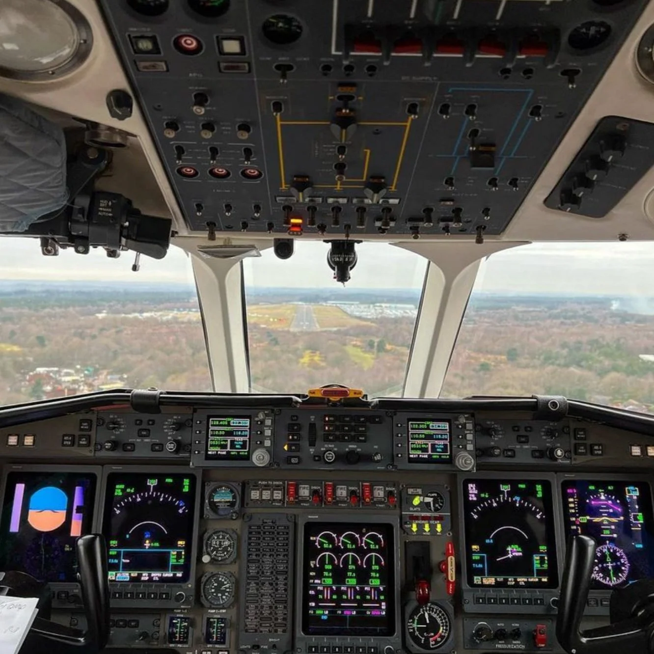 Cockpit view from a commercial airplane showing various flight instruments, gauges, and screens with a view of the runway and landscape ahead.