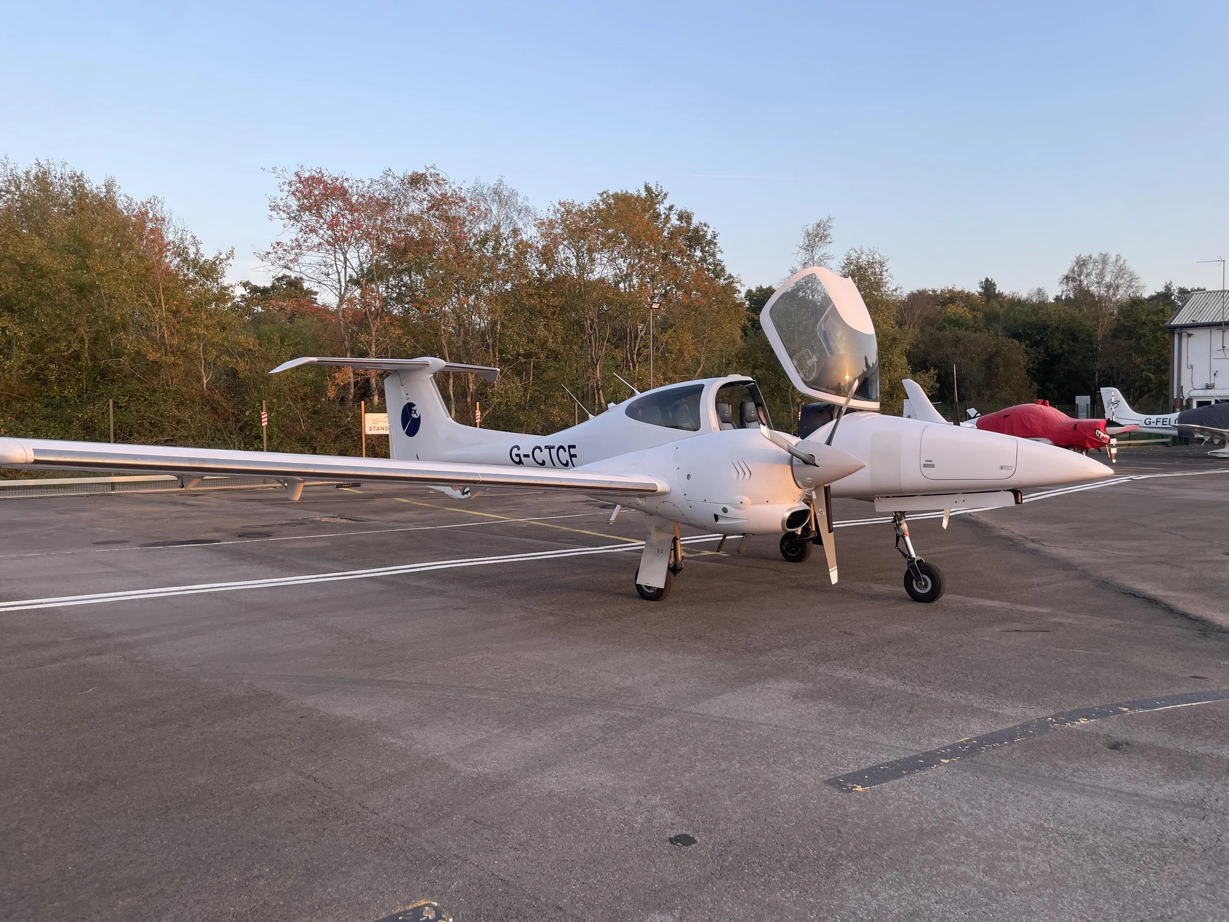 Small white aircraft on runway with open canopy and trees in the background