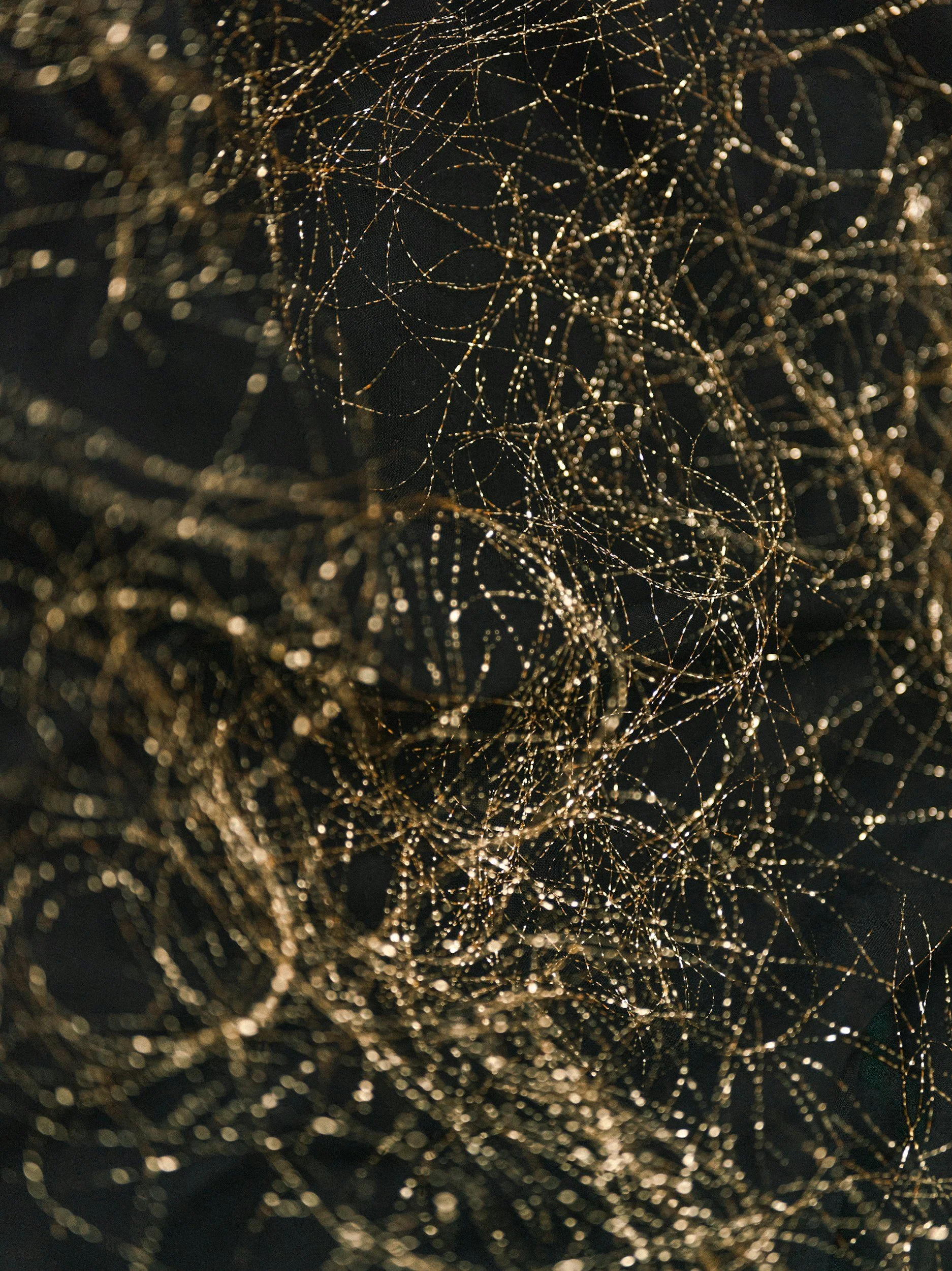 Close-up of tangled, shimmering gold and black metallic threads or wires against a dark background.