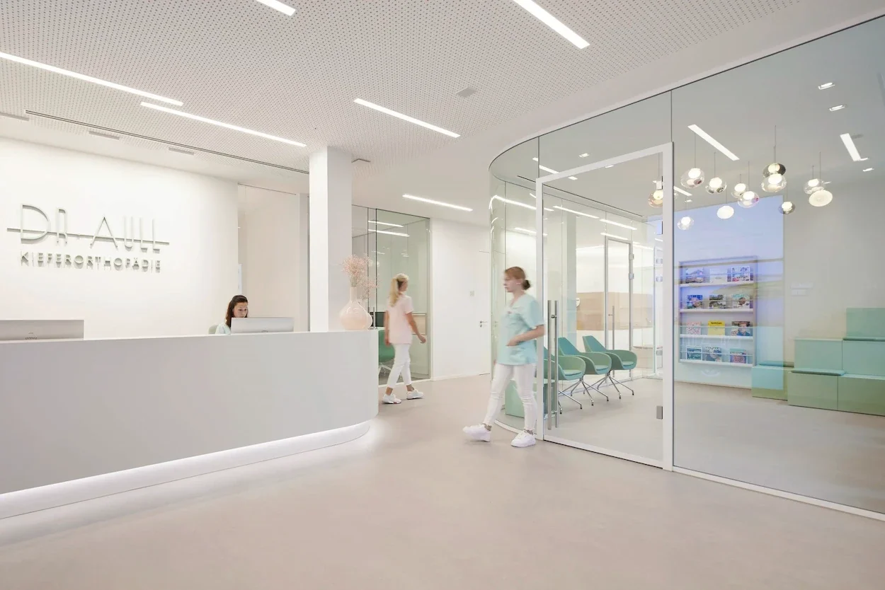 Moderner Empfang einer Kieferorthopädie mit verglastem Wartebereich, heller Praxiseinrichtung und maßgefertigter Theke