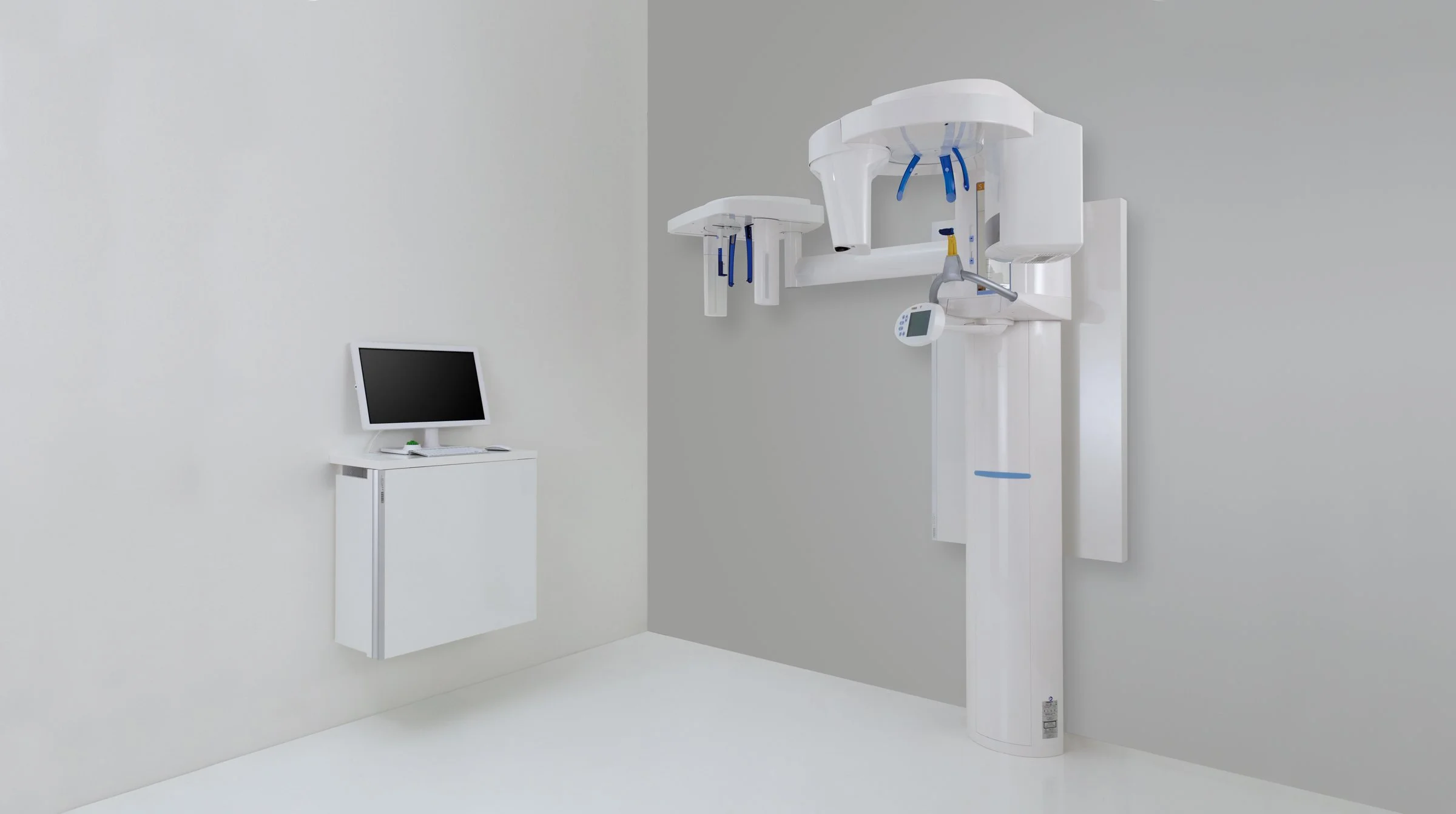 Ein modernes Zahnarztlager mit einem digitalen Röntgengerät an der Wand und einem kleinen Monitor auf einer weißen Ablage.