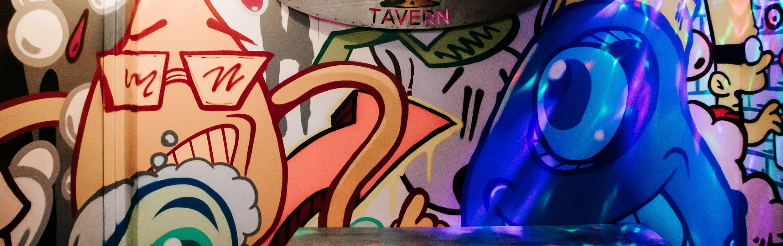 Colorful graffiti art featuring cartoon characters, abstract shapes, and vibrant lighting effects.