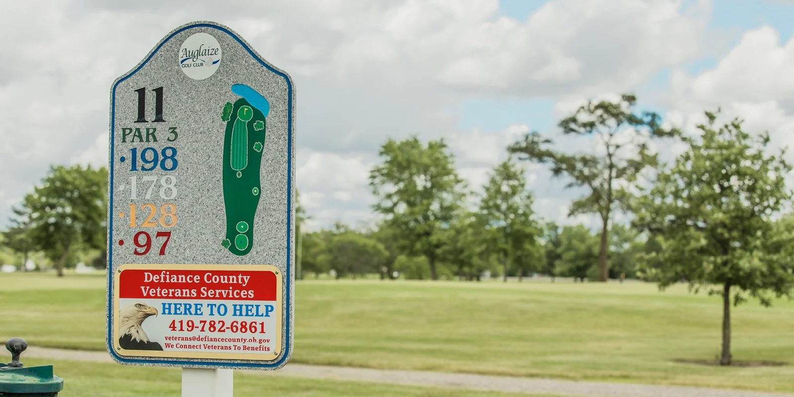 Golf course sign for Hole 11, a Par 3, at Auglaize Golf Club, with yardage options listed from 198 yards to 97 yards, and a section for Defiance County Veterans Services with contact information and an image of an eagle.