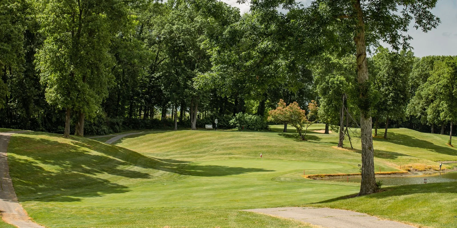 A golf course with lush green grass, trees, and a small water hazard near the green.