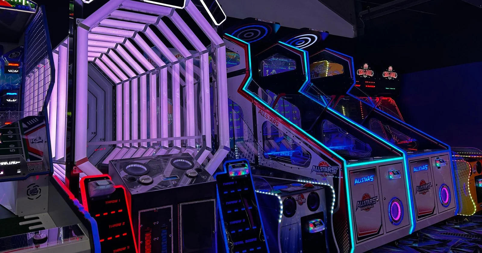 A colorful arcade game area with illuminated pinball machines and electronic games featuring neon lights and a dark background.