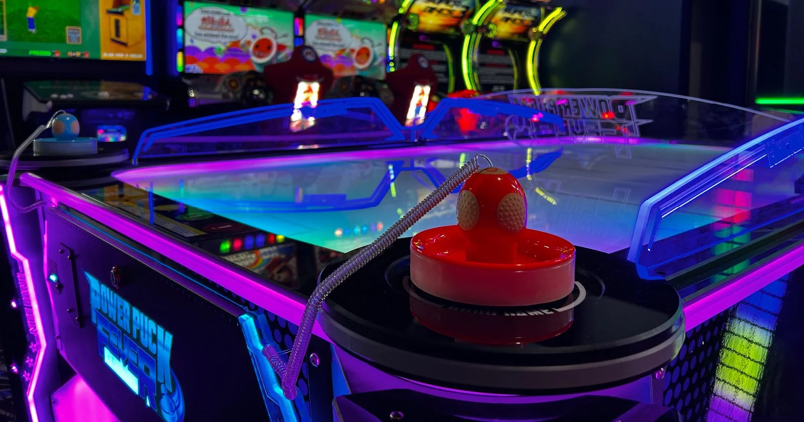A neon-lit arcade with a pinball machine featuring colorful lights and a red bumper in the foreground.