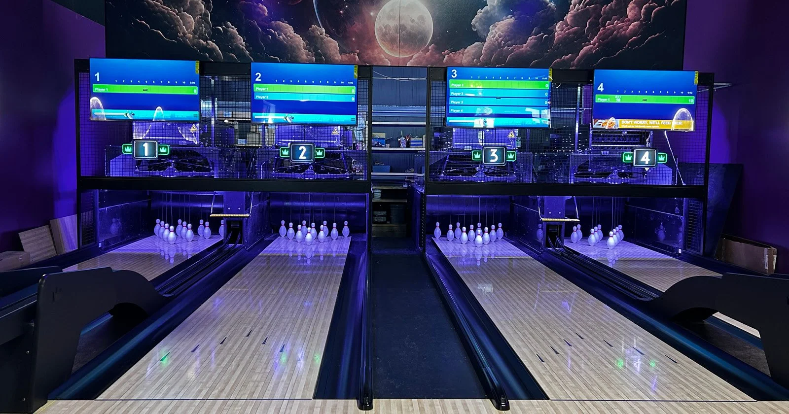 Bowling lanes with digital score screens, bowling pins arranged at each lane, and neon purple lighting in the background.