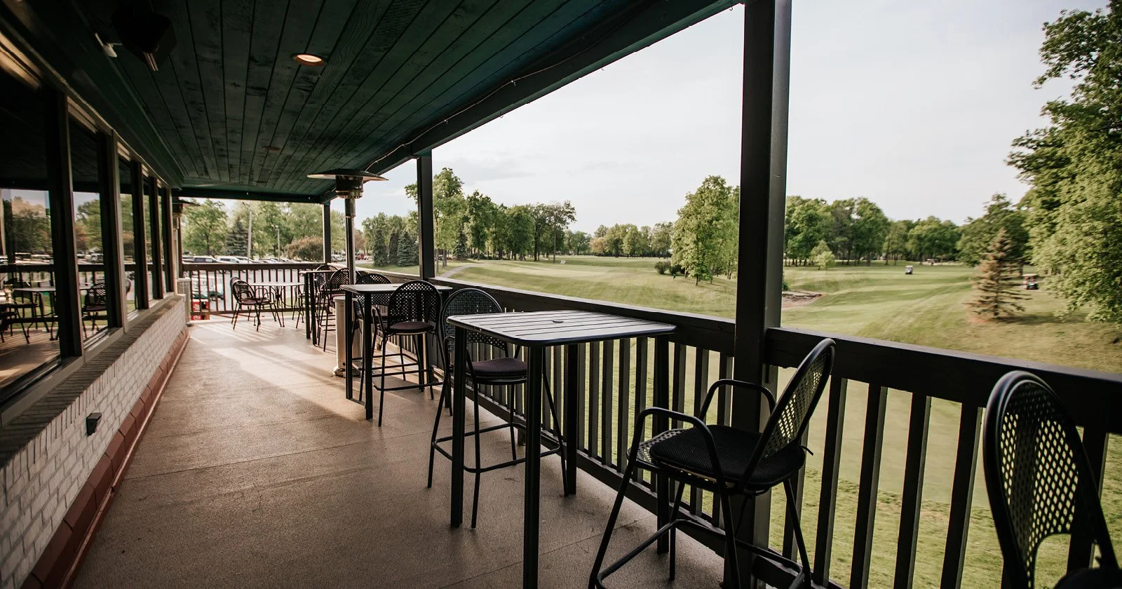 Empty outdoor patio with black tables and chairs overlooking a golf course.