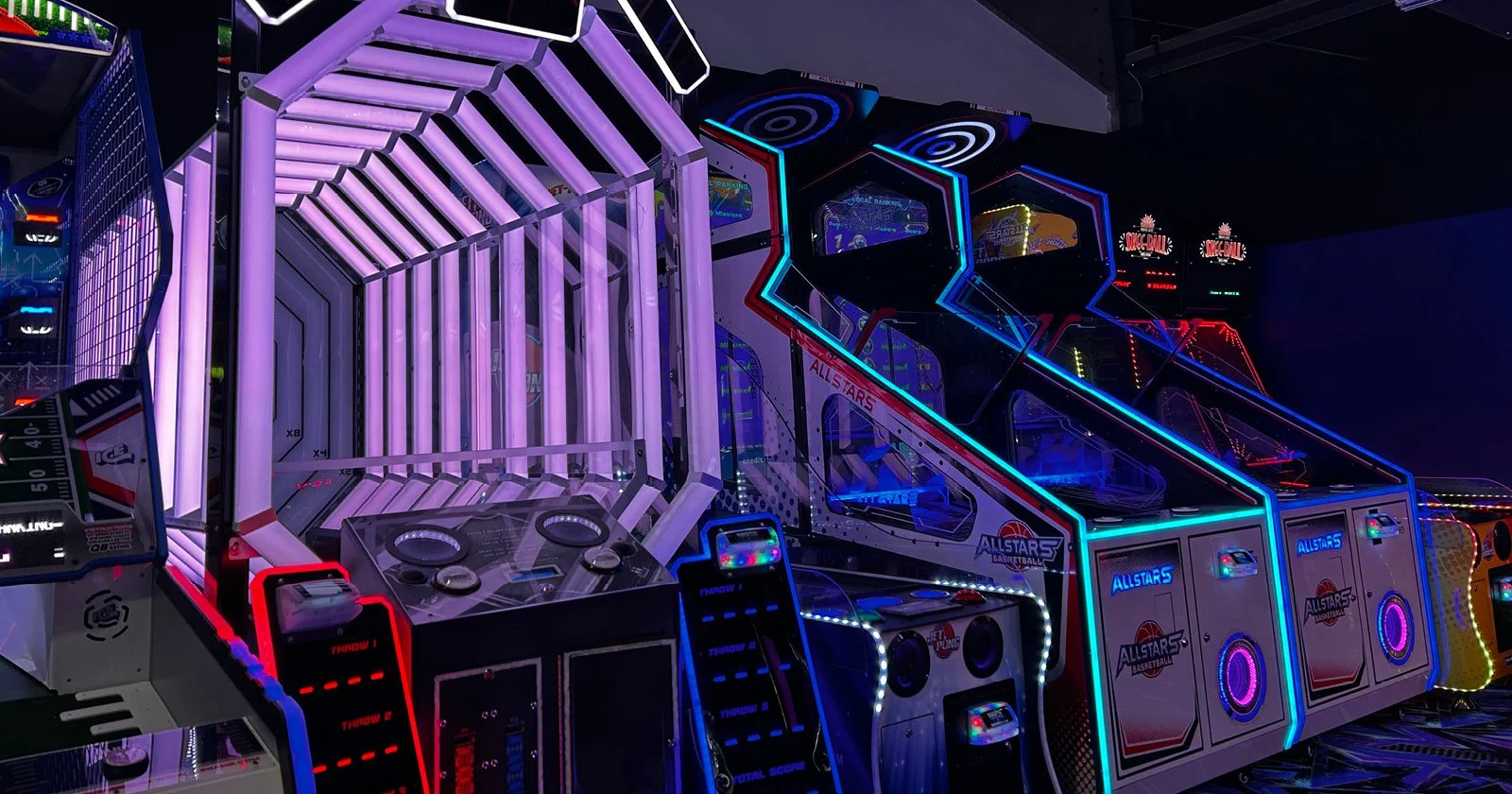 Multiple arcade basketball games with neon lights at an arcade.