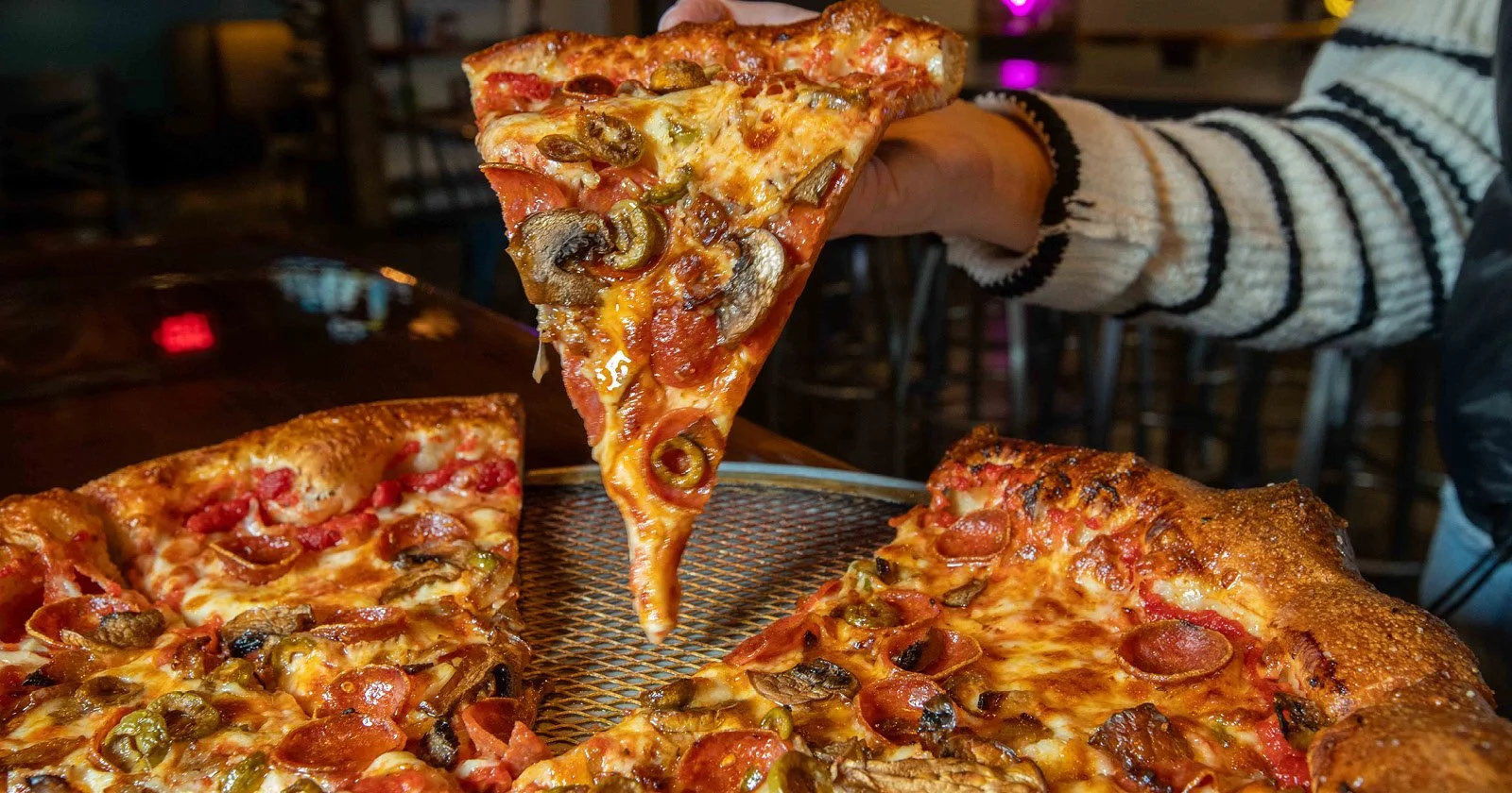 Slice of pepperoni pizza with mushrooms and green peppers being lifted from a pizza box