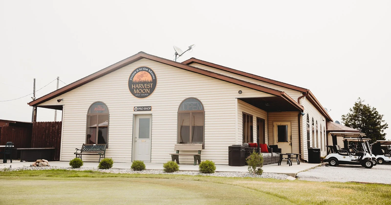 A golf course clubhouse with a sign that reads 'Harvest Moon Golf Course' and a small parking lot with golf carts.