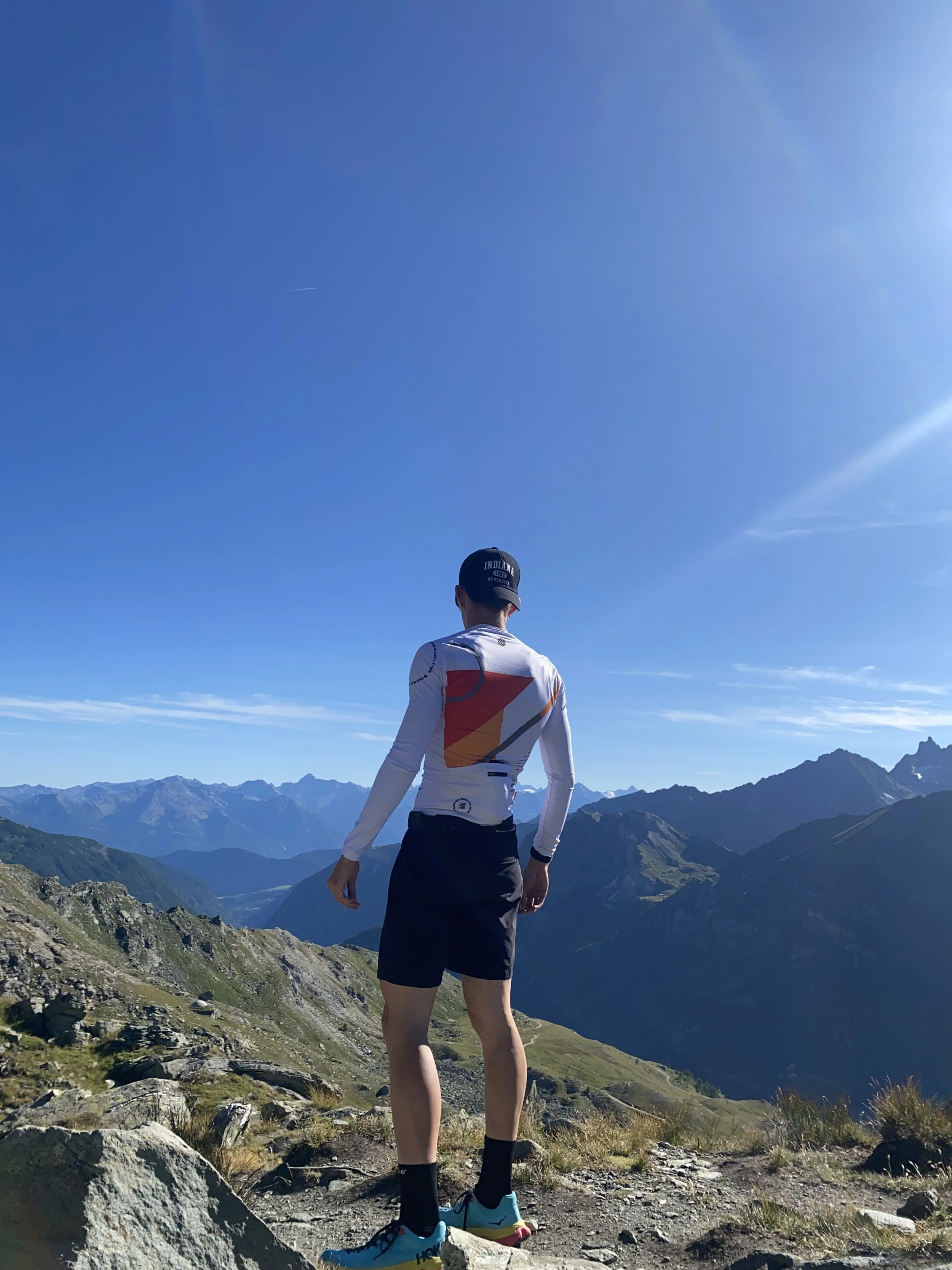 Uomo che si trova in una montagna con paesaggi di montagne e cielo blu sullo sfondo.