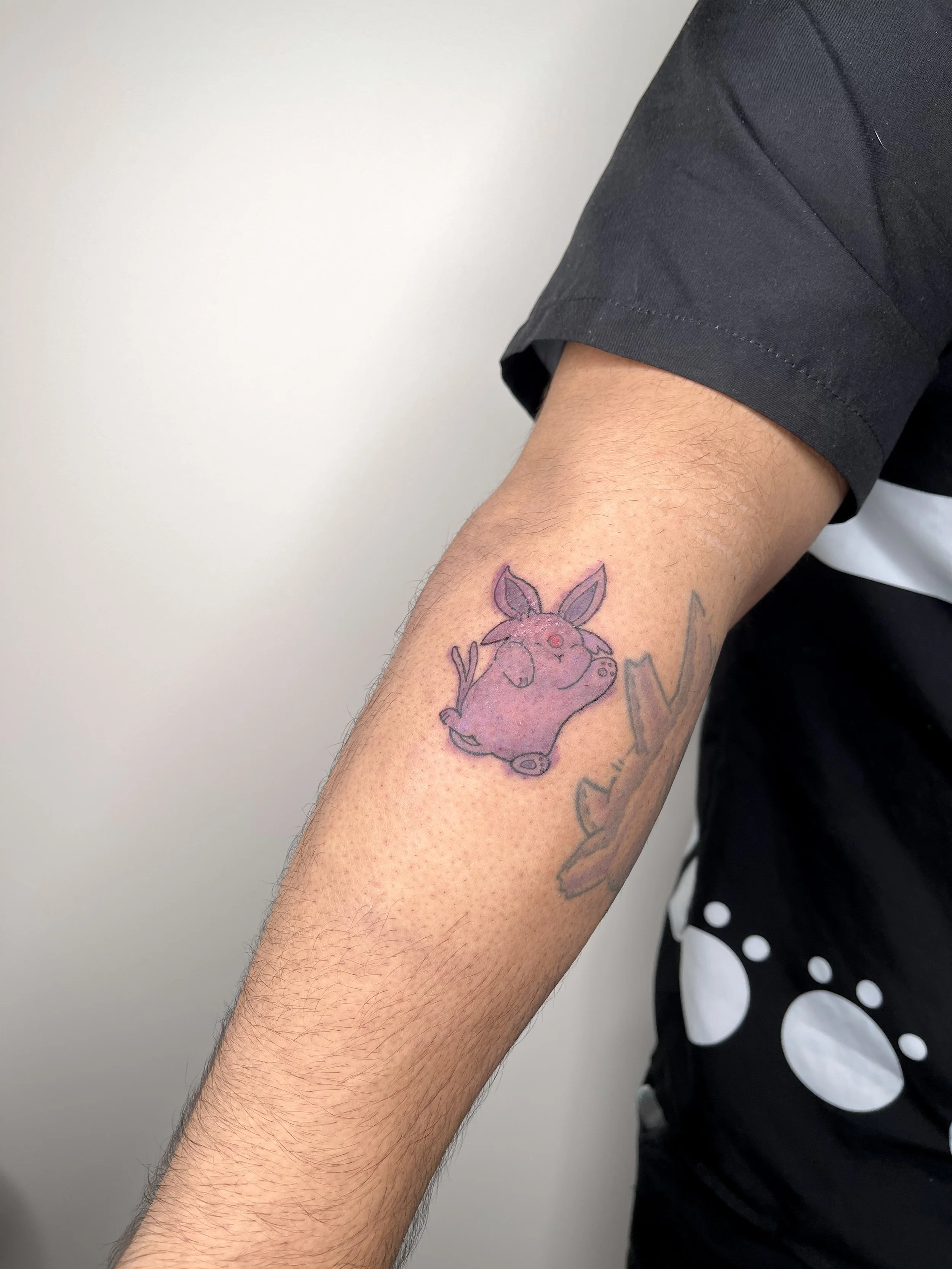 A tattoo of a purple watercolor-style espeon on a person's forearm.