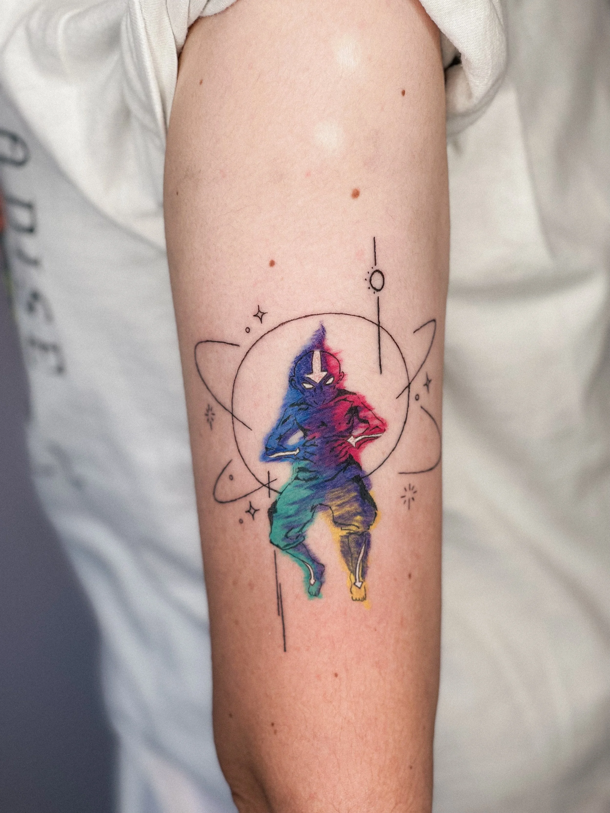 Colorful tattoo of Avatar the Last Airbender, surrounded by geometric and star designs on the upper arm.