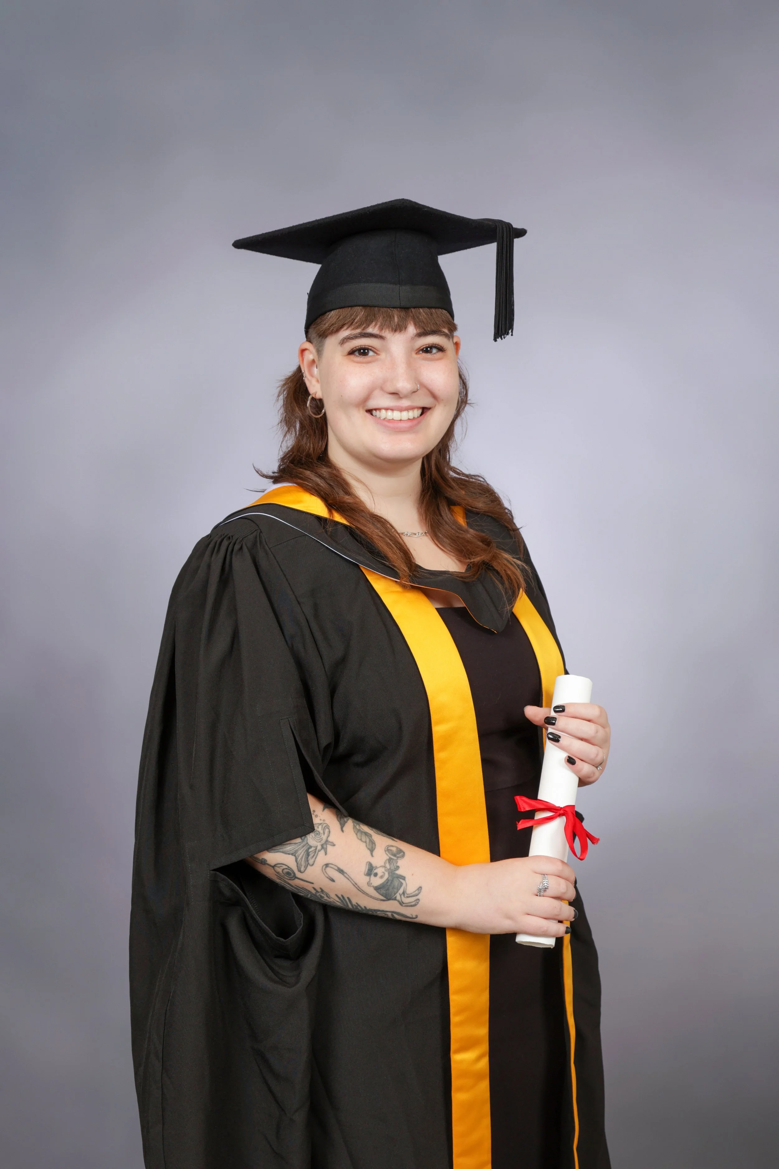 Joelle in graduation cap and gown holding a diploma with a red ribbon, smiling for the camera.