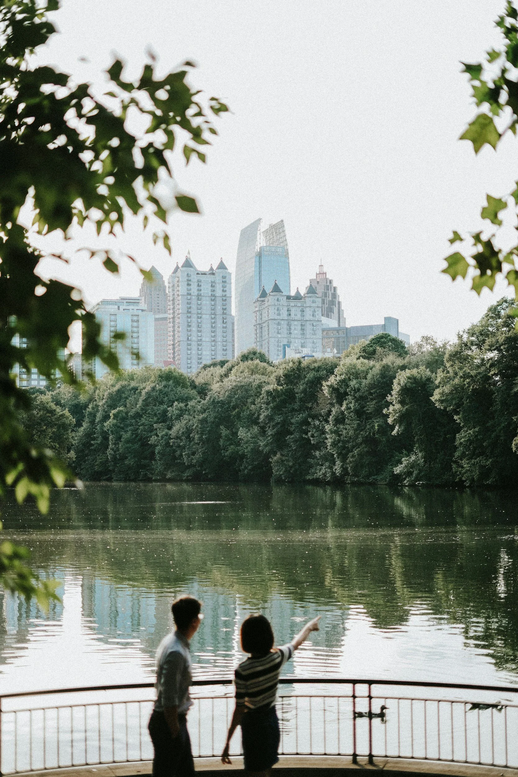 People near a body of water with trees and a city skyline in the background.