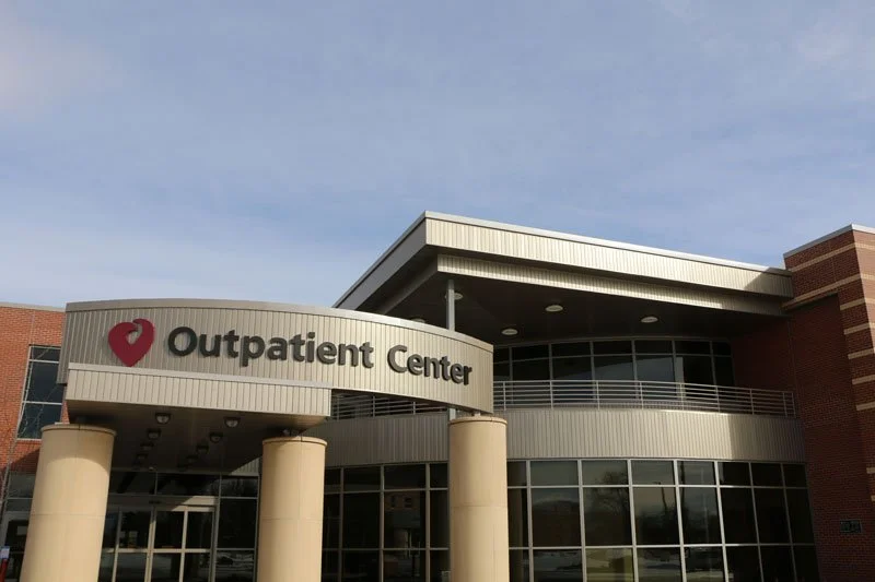 Exterior of a hospital outpatient center with a rounded entrance, large windows, and a sign that reads 'Outpatient Center' with a heart-shaped logo.