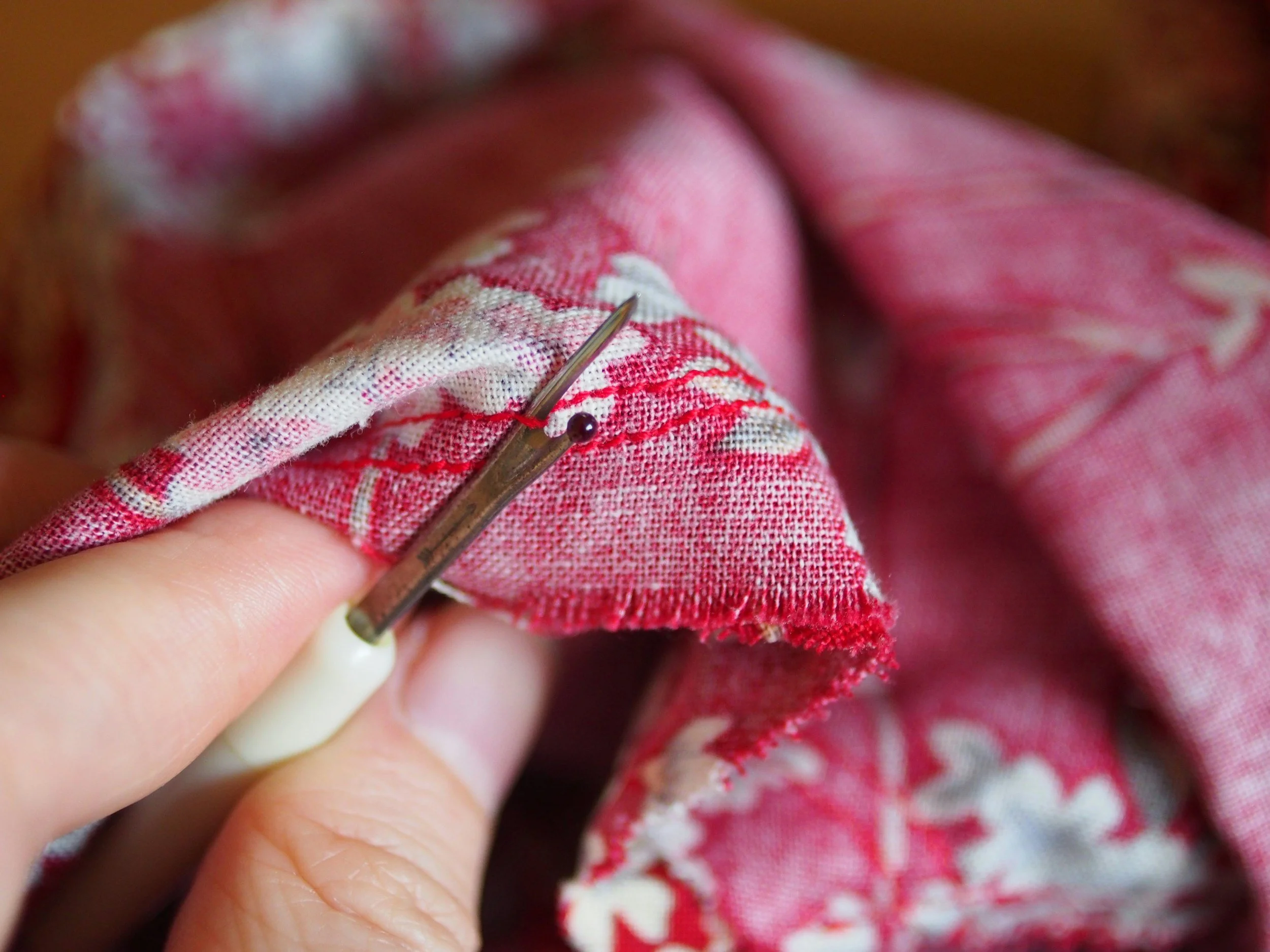 hand using a seam ripper to undo stitching on pink and white cloth