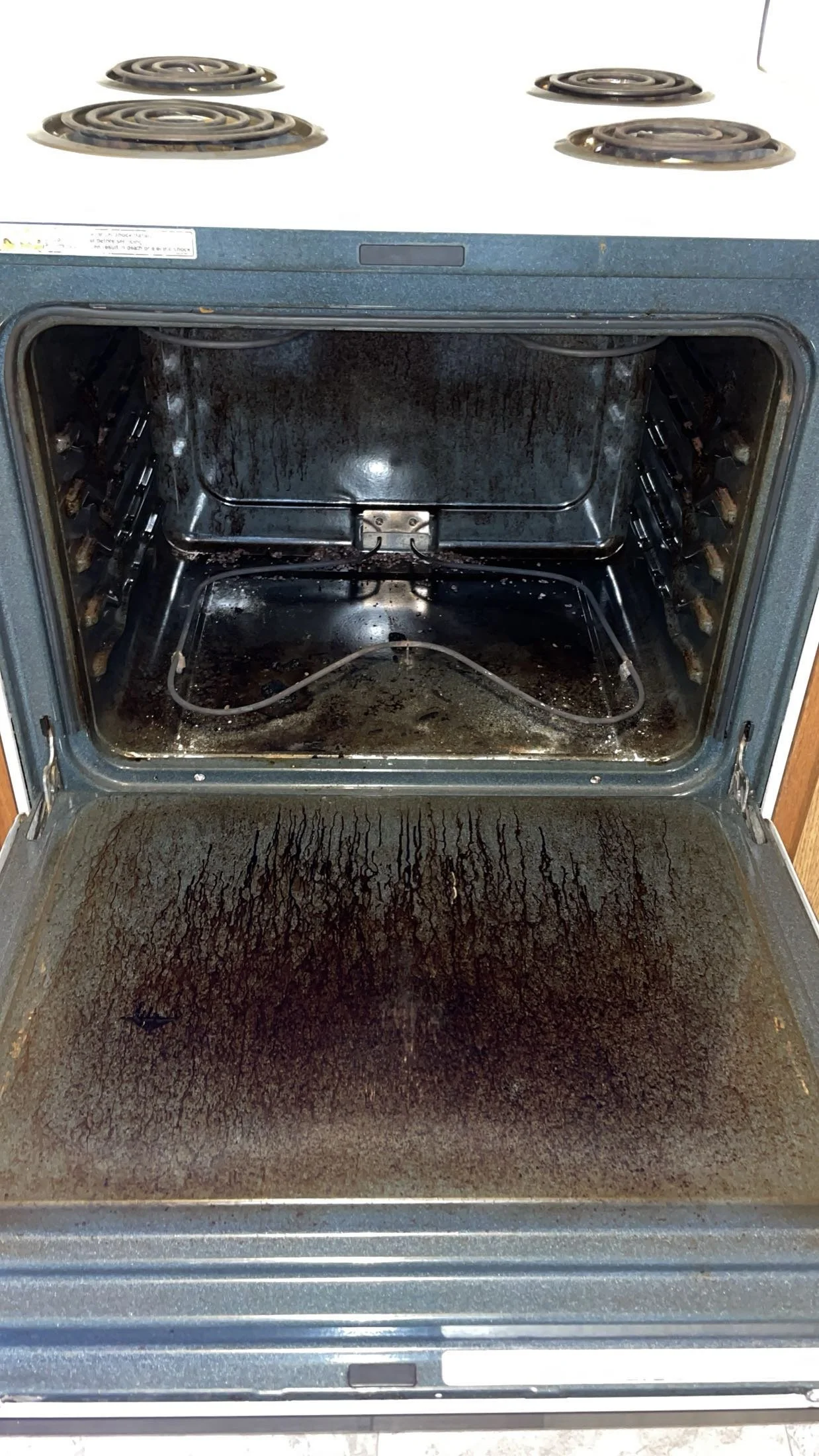 The oven door is open and the interior of the oven is very dirty, with burnt food and grease on the bottom and sides.