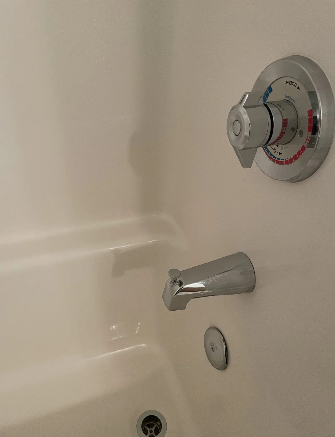 Empty bathtub with a silver faucet and a wall-mounted dial for controlling water temperature and flow.