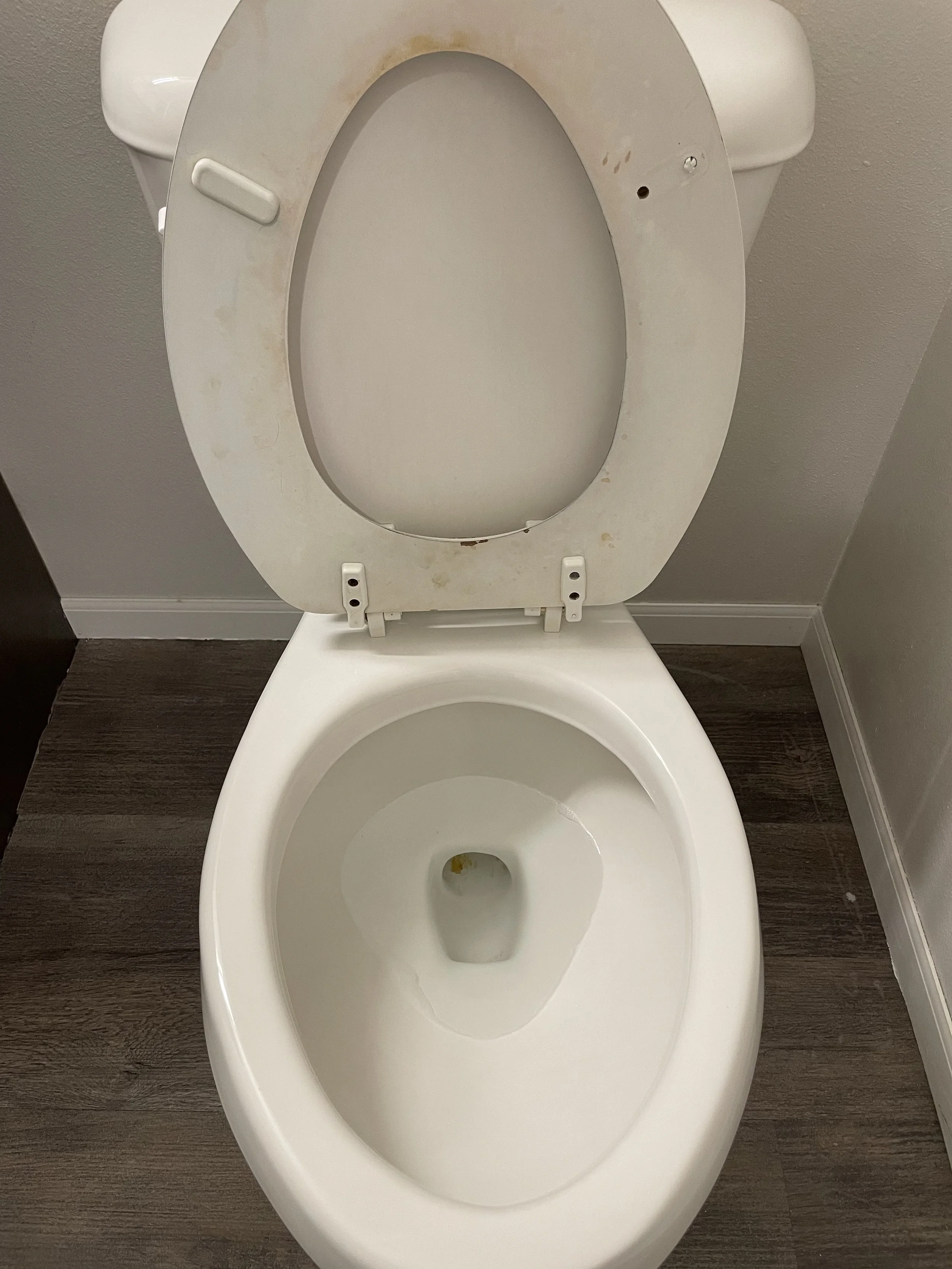 A toilet bowl with the lid raised, showing some stains and dirt inside the bowl and on the rim.