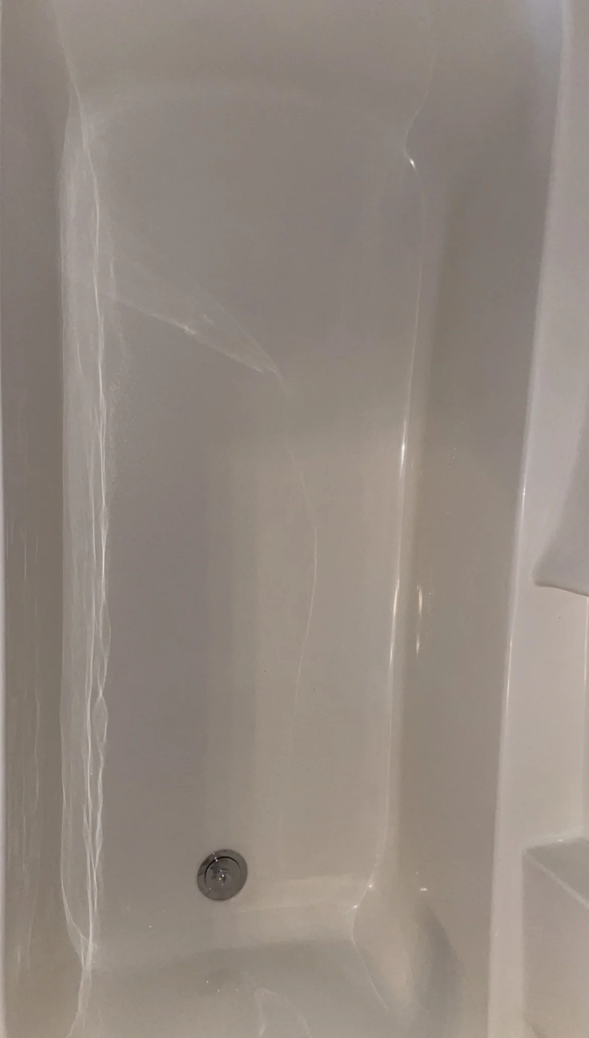Empty bathtub with a drain at the bottom and smooth white walls