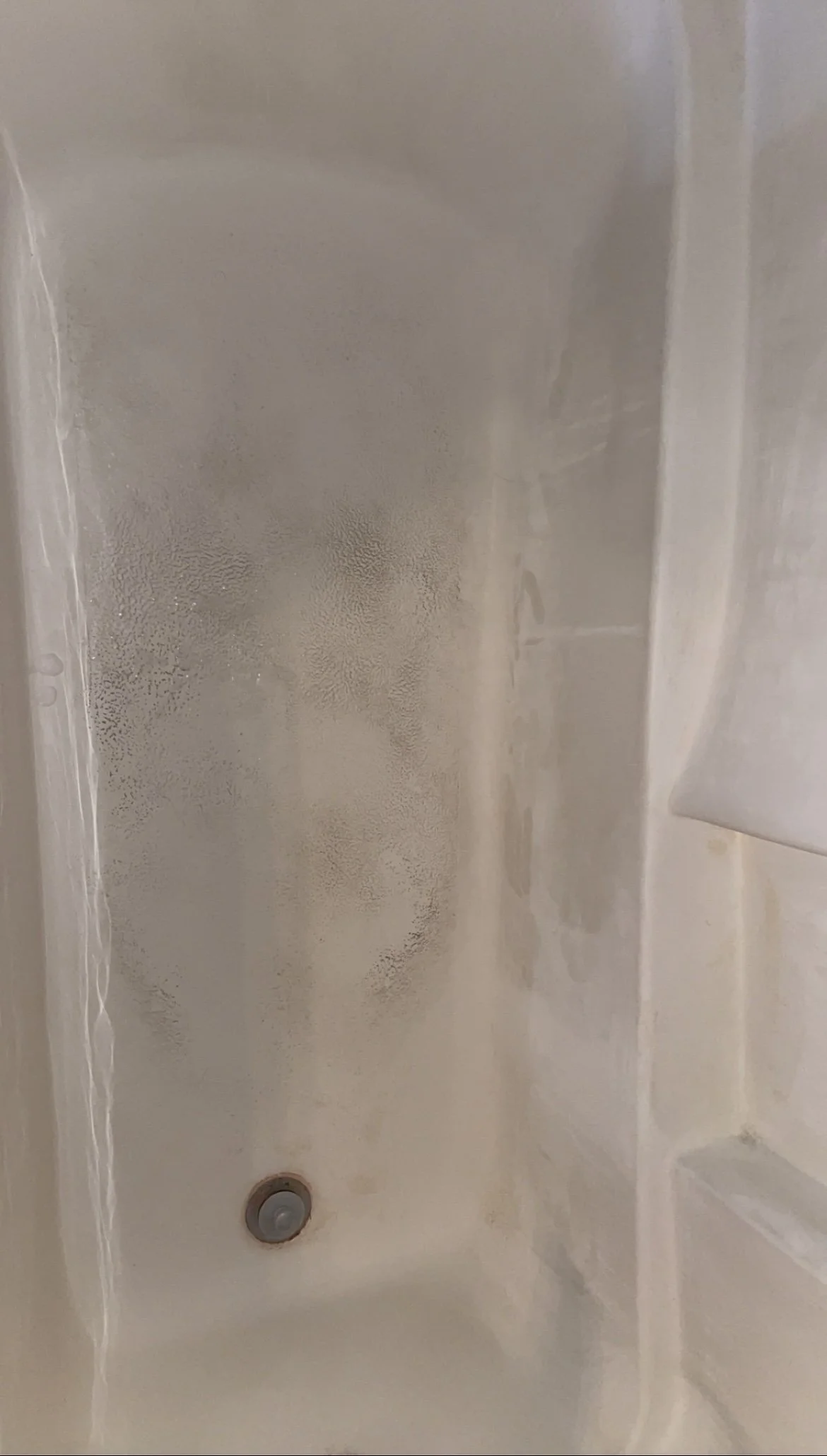 A shower stall with a frosted glass door, a drain at the bottom, and water droplets on the glass surface.
