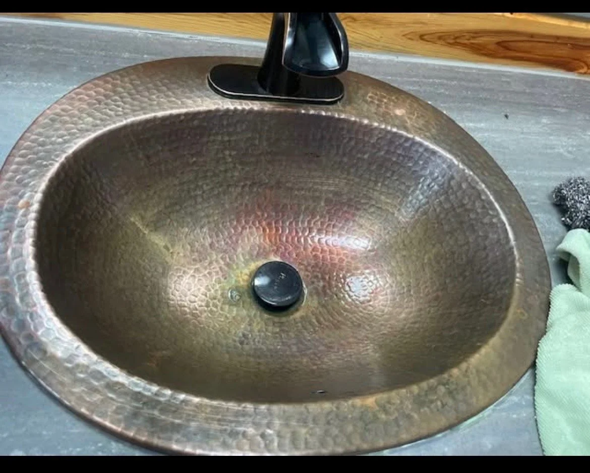 A hammered copper bathroom sink with a black faucet.