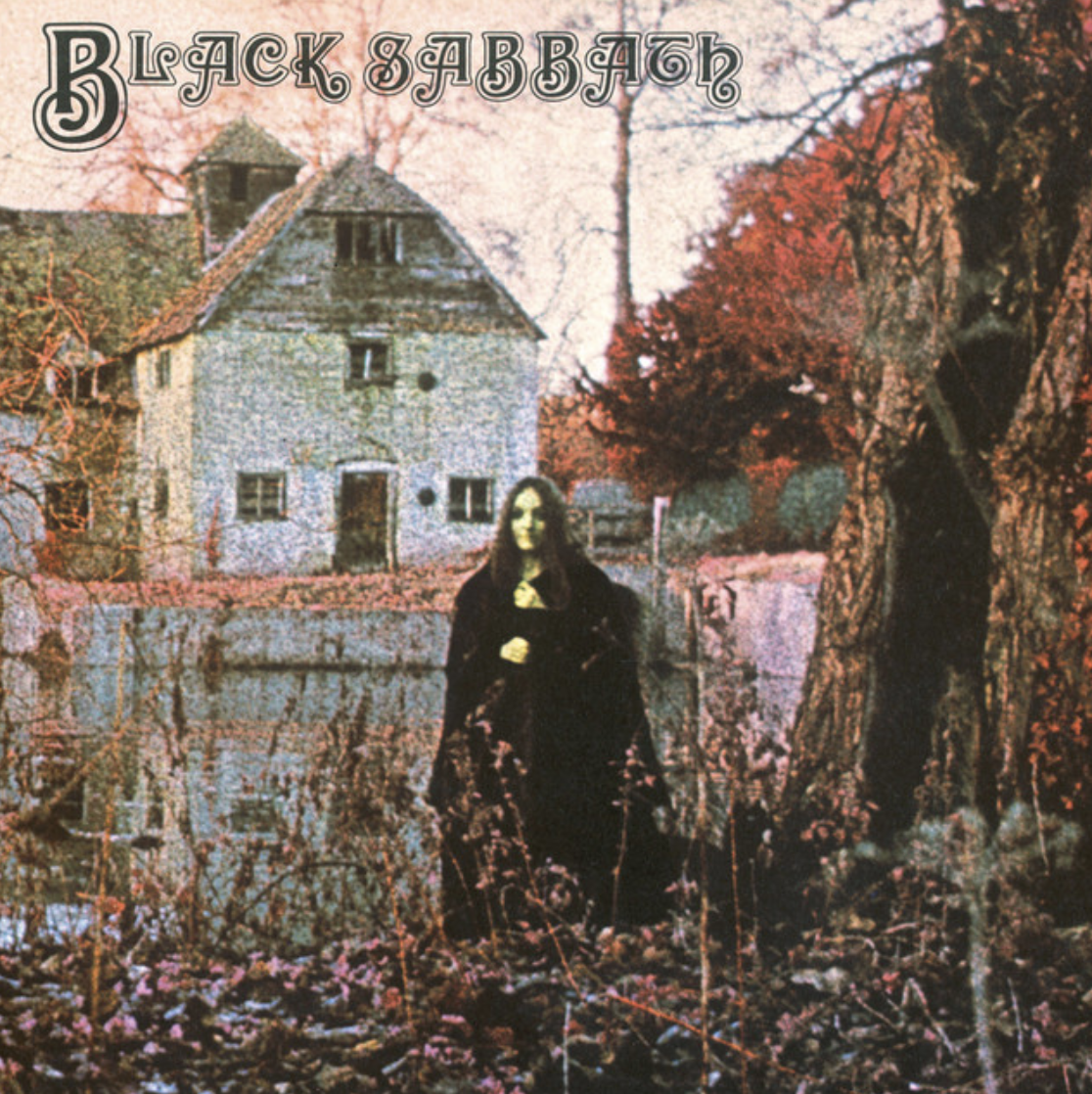 Album cover art for Black Sabbath featuring a woman with long hair in a dark dress standing in a wooded area near a pond, with an old house and trees with autumn leaves in the background.