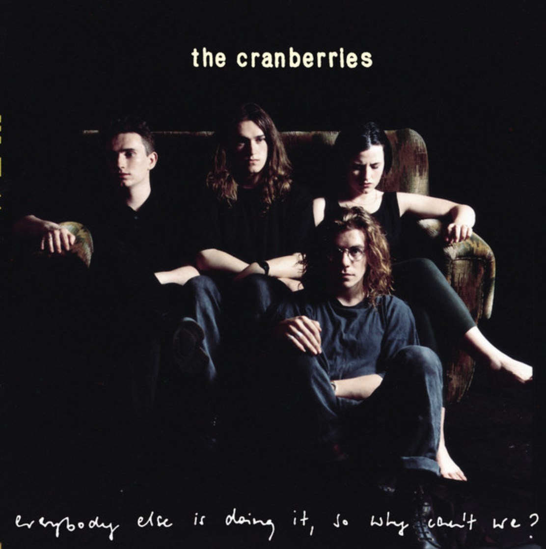 The album cover for the band The Cranberries, featuring four band members sitting on a dark background with a vintage sofa and the text "the cranberries" at the top and the handwritten phrase "everybody else is doing it, so why can't we?" at the bottom.