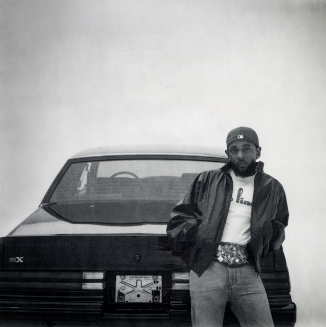 A man wearing a baseball cap and a leather jacket standing in front of a car.
