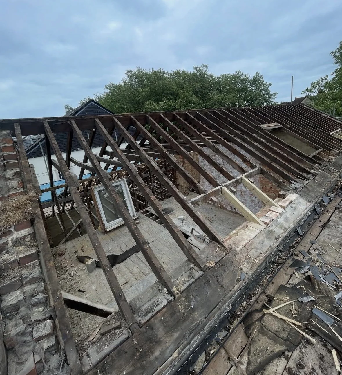 Roof of a building under renovation with missing shingles, exposed wooden beams, and construction debris scattered around. - CPS ROOFING IMAGE