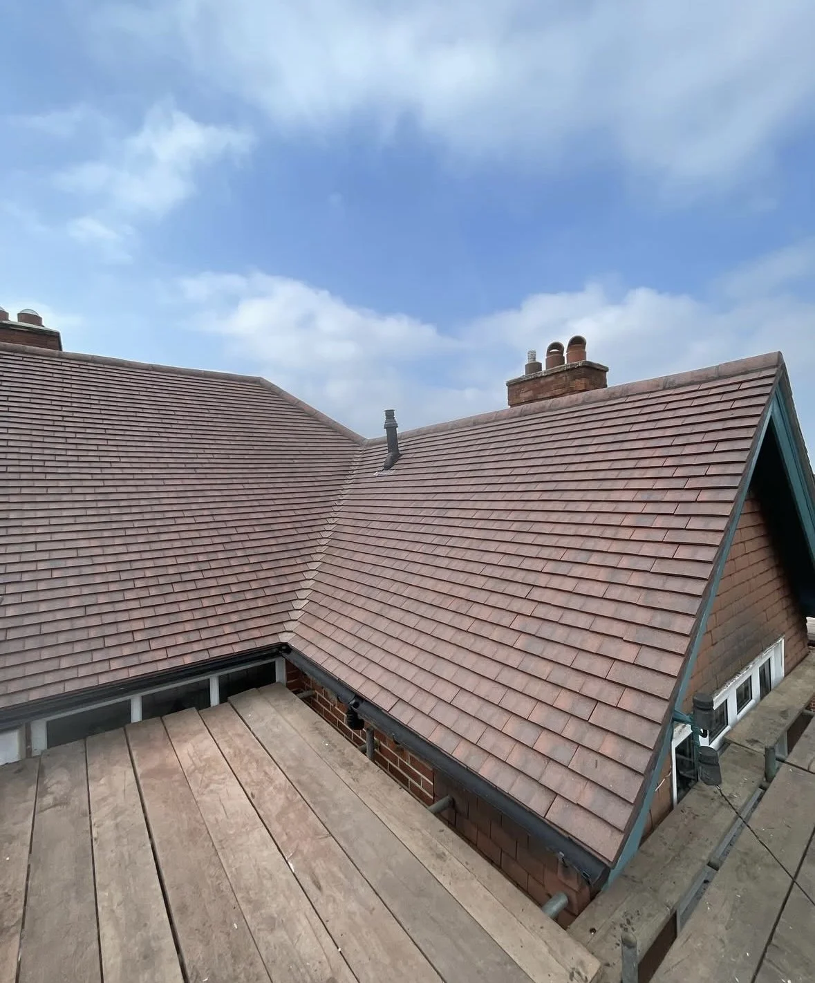 View of a house roof with reddish-brown shingles, seen from a deck or balcony under a cloudy sky. CPS ROOFING IMAGE