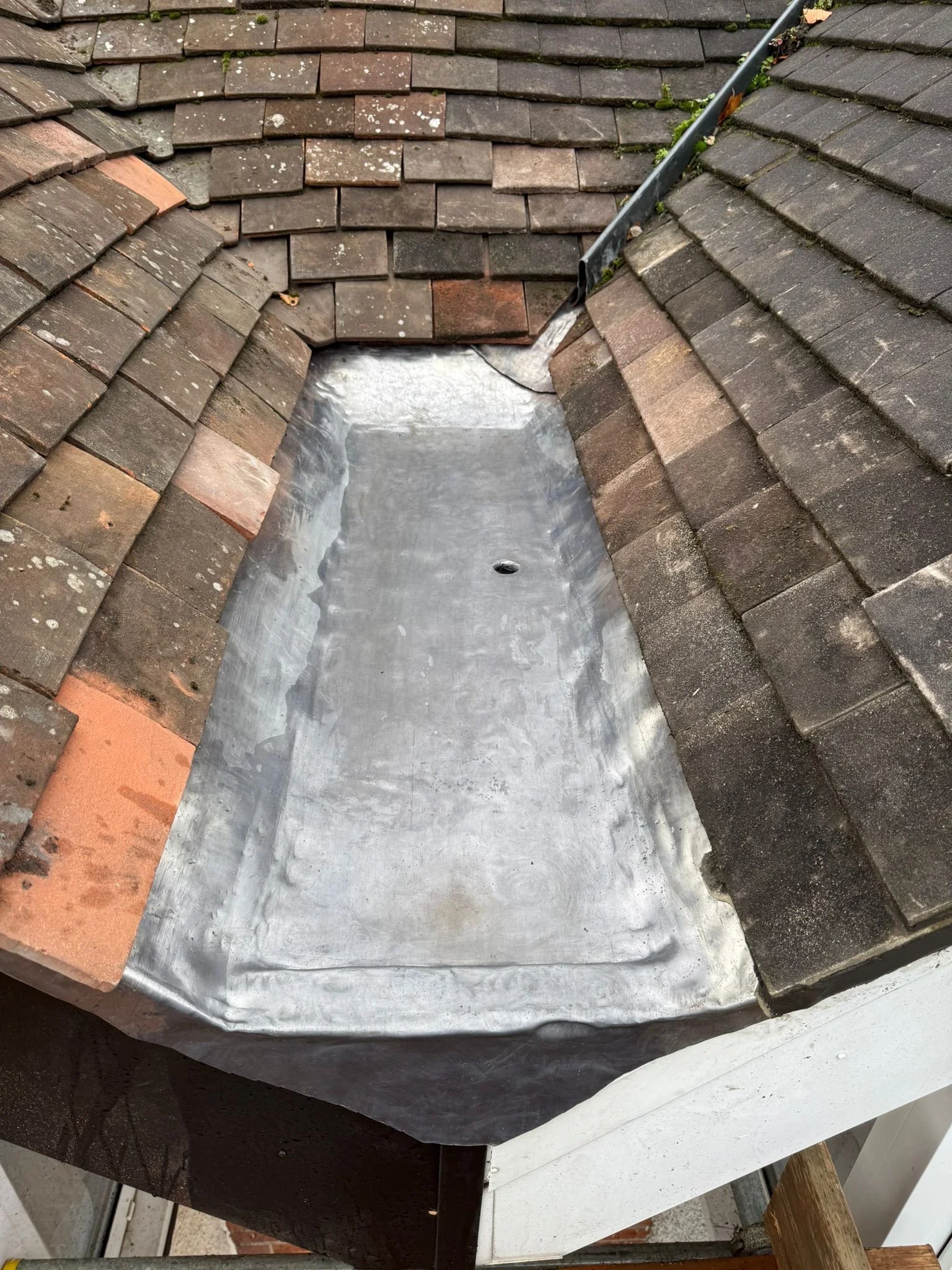 A roof with old, weathered shingles and a new metal flashing installed around a small dormer window section to prevent leaks.