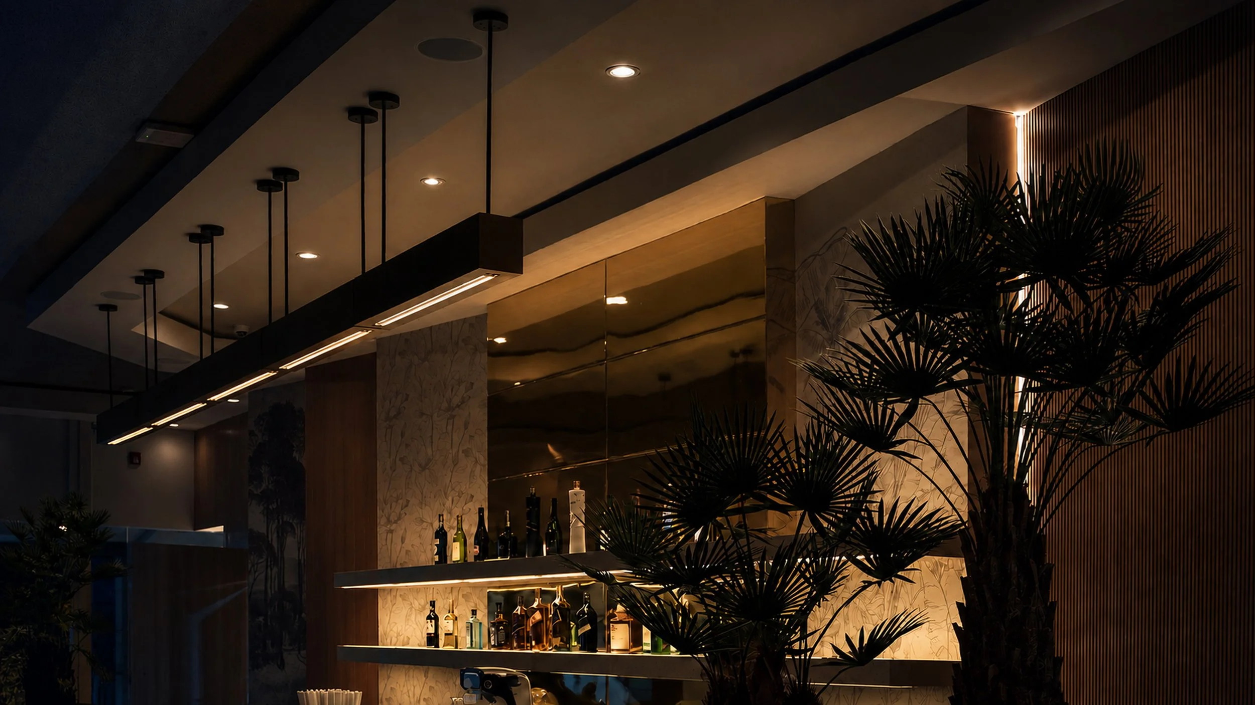 Interior moderno con barra de bebidas, paredes de mármol y plantas decorativas, iluminación cálida y iluminación empotrada en el techo.