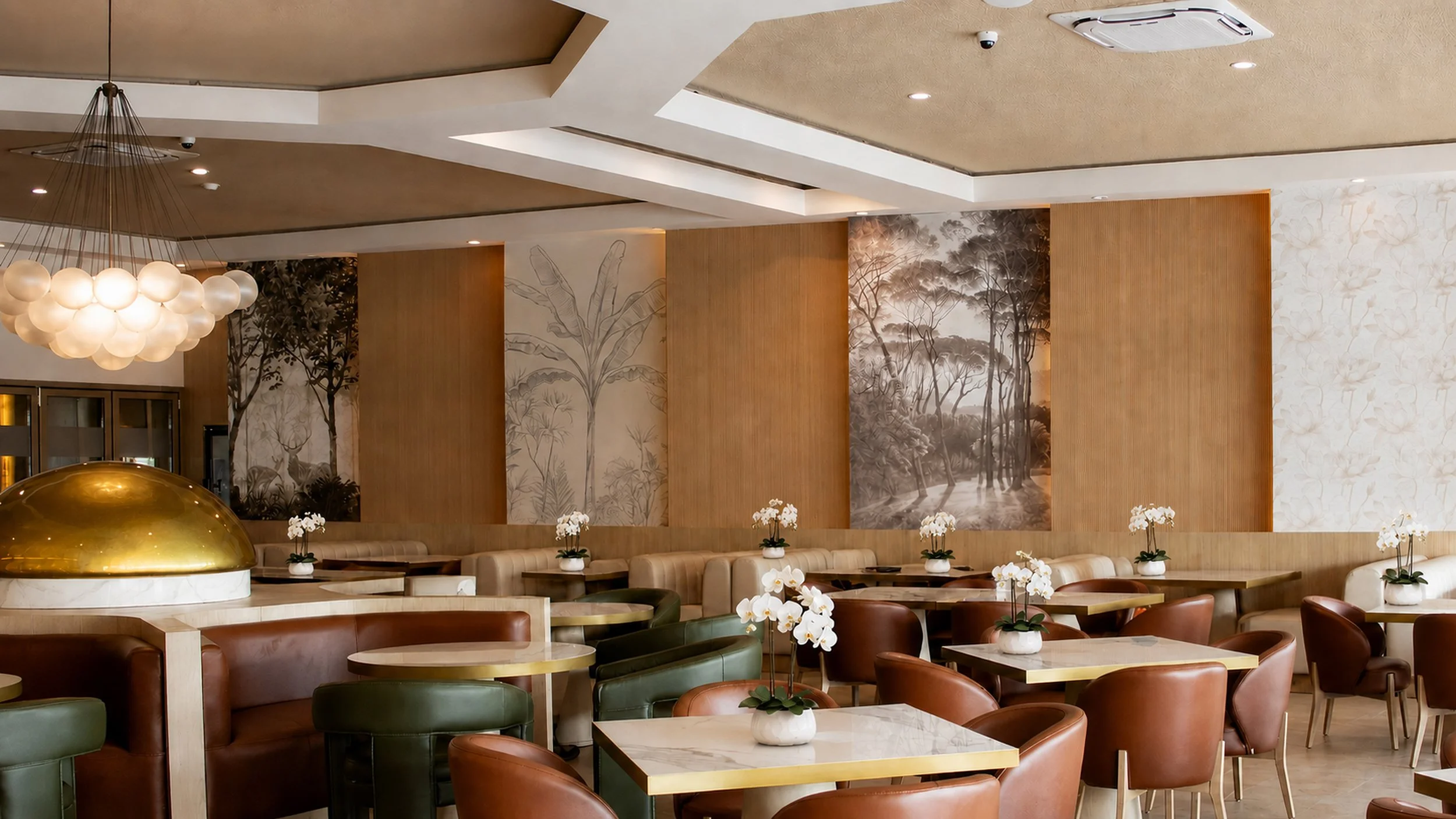 Interior de un restaurante elegante con paredes decoradas con pinturas de árboles y plantas, mesas con flores blancas y sillas de cuero en tonos marrón y verde, y una lámpara colgante moderna con globos de luz.