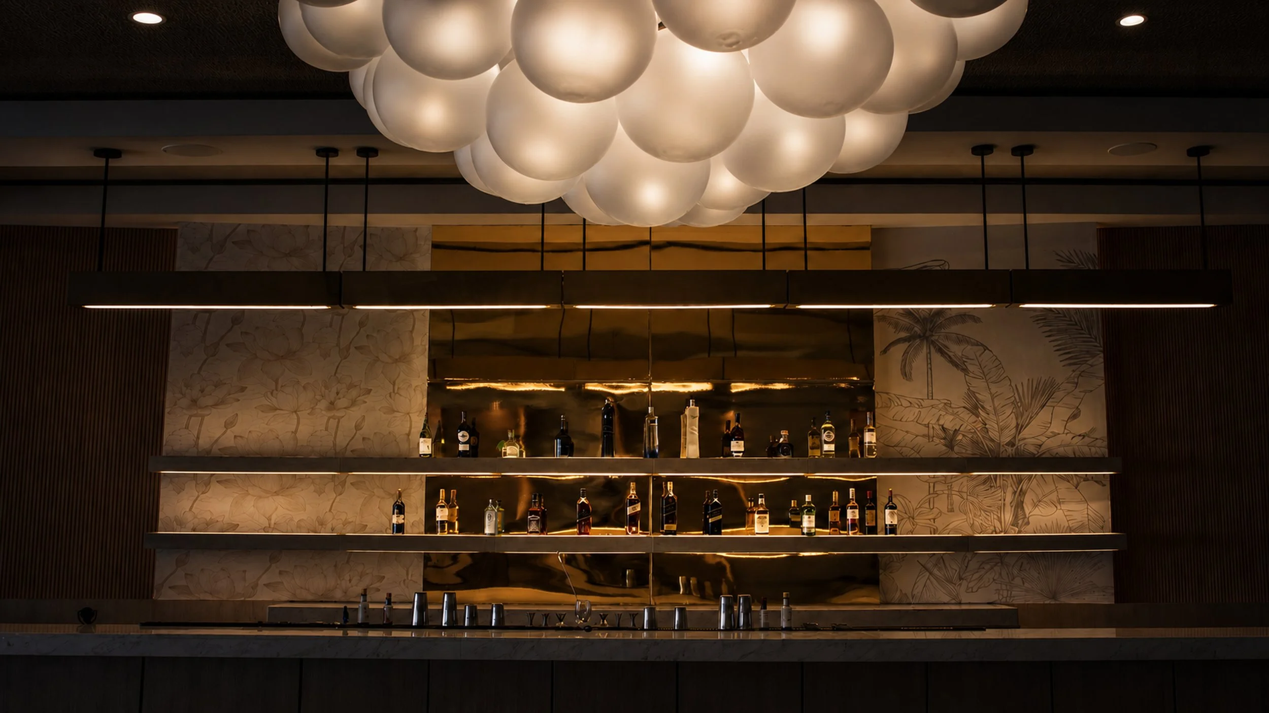 Bar con decoración de lámparas de globos blancos en el techo y estantería con botellas de alcohol.