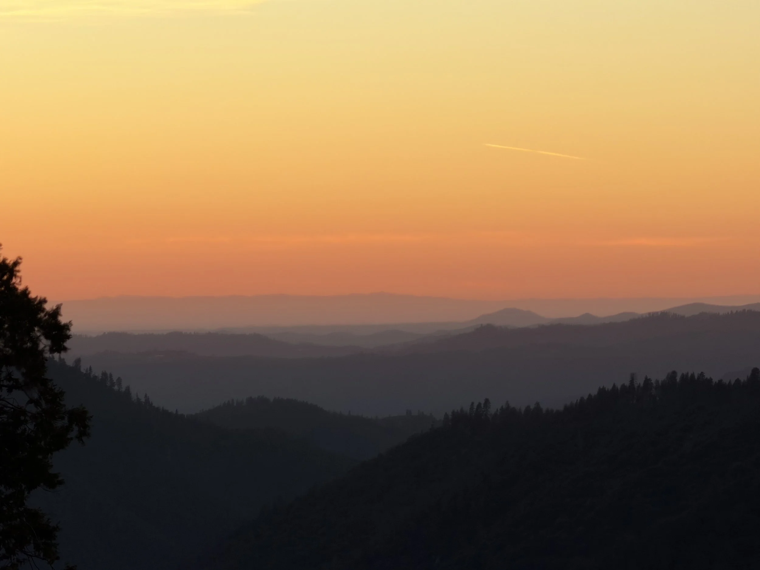 Sunset over layered silhouette mountains with a pastel yellow, orange, and pink sky.