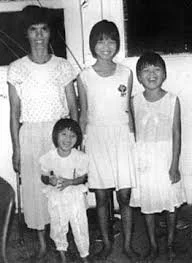 Black-and-white photo of missing girl Jie Zhao Li with her mother and two sisters, standing indoors and smiling.
