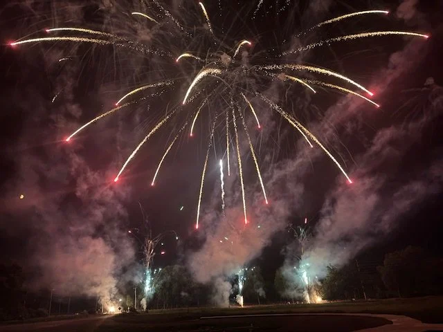Fireworks exploding in the night sky, with colorful streaks and smoke over an open outdoor area.