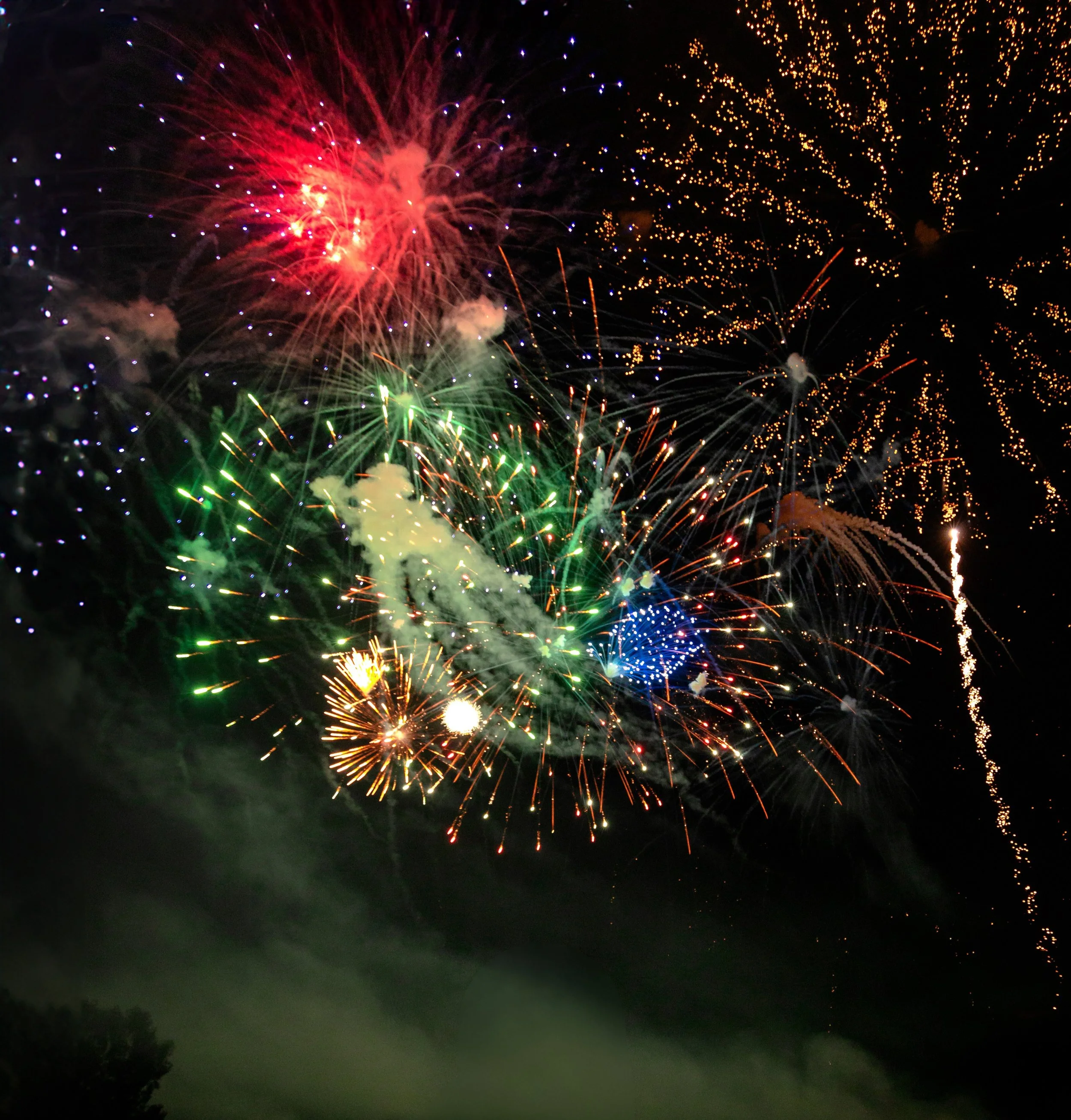 Colorful fireworks exploding in the night sky with green, red, blue, yellow, and purple lights