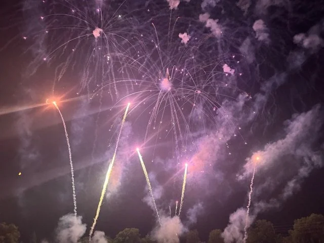 Colorful fireworks exploding in the night sky with smoke and trees at the bottom.