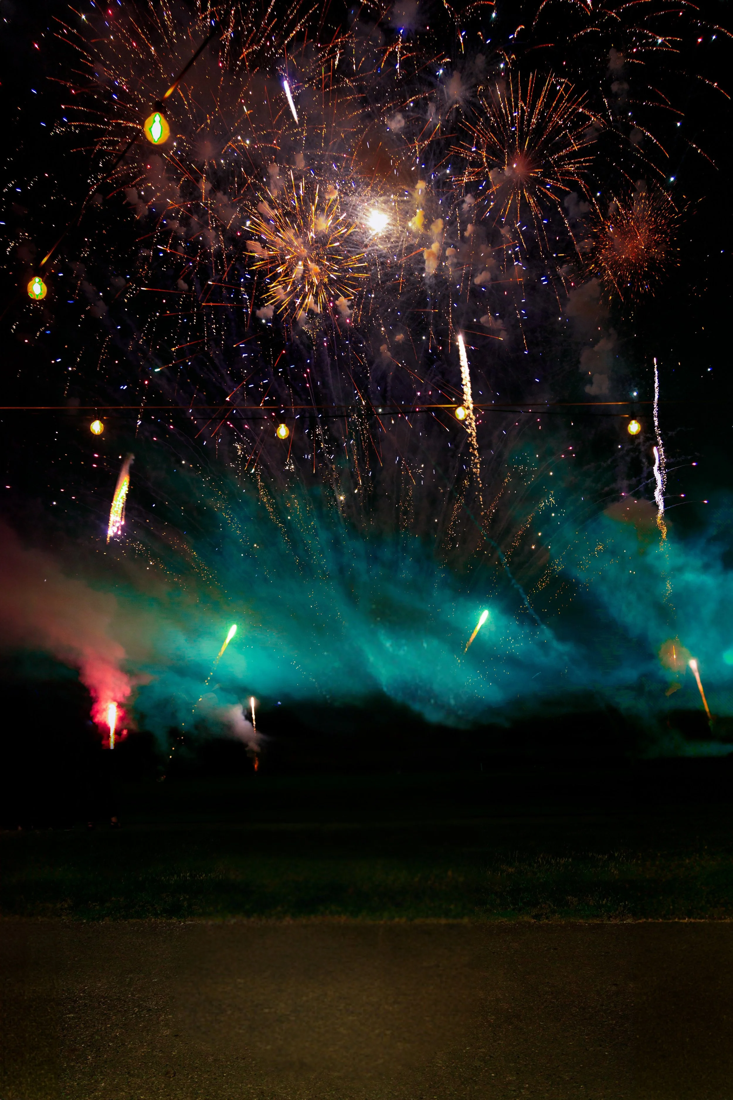 Fireworks lighting up the night sky with colorful explosions and smoke on the ground.