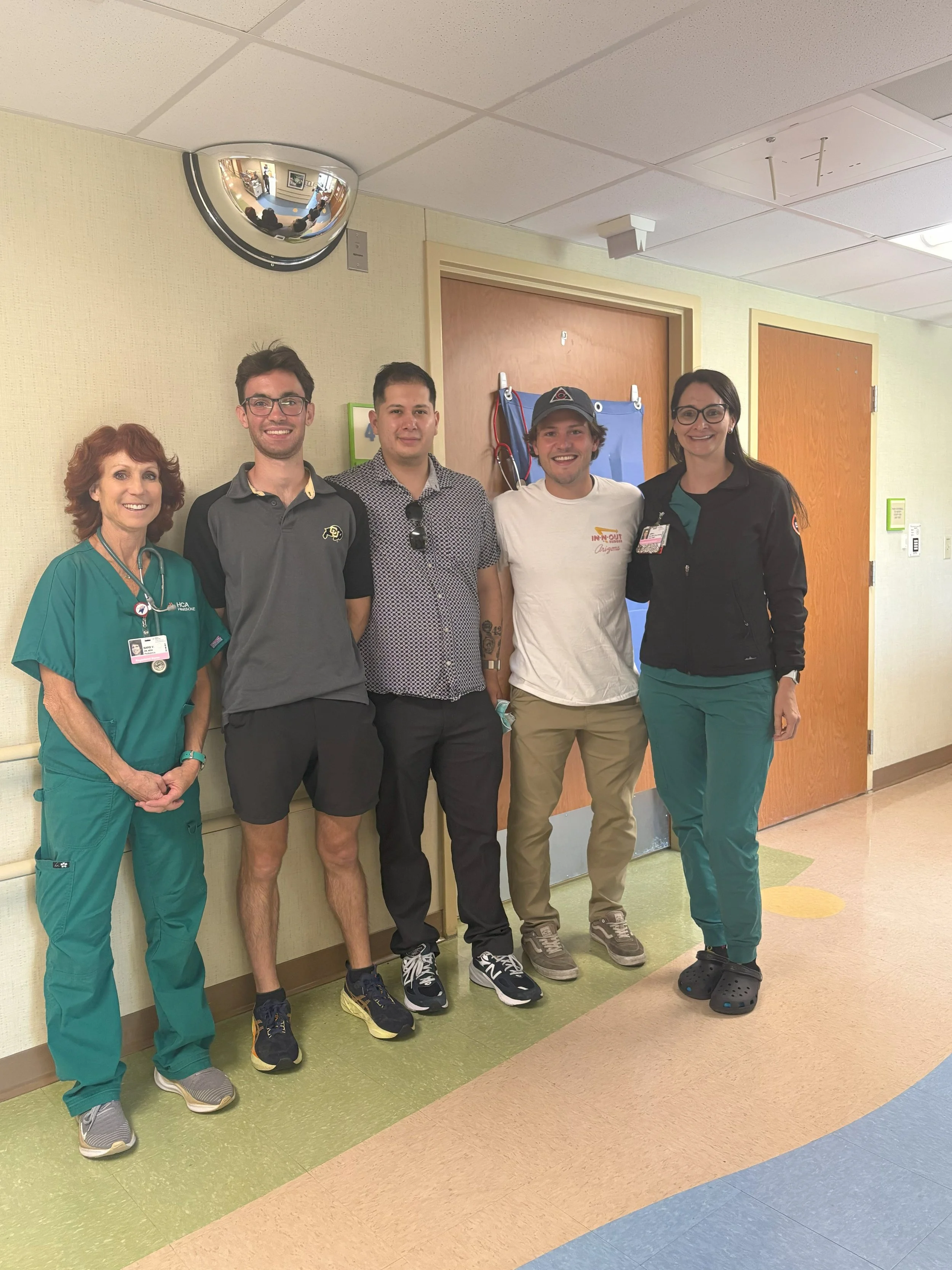 Group of five people standing in a hospital corridor, including nurses and patients, smiling at the camera.